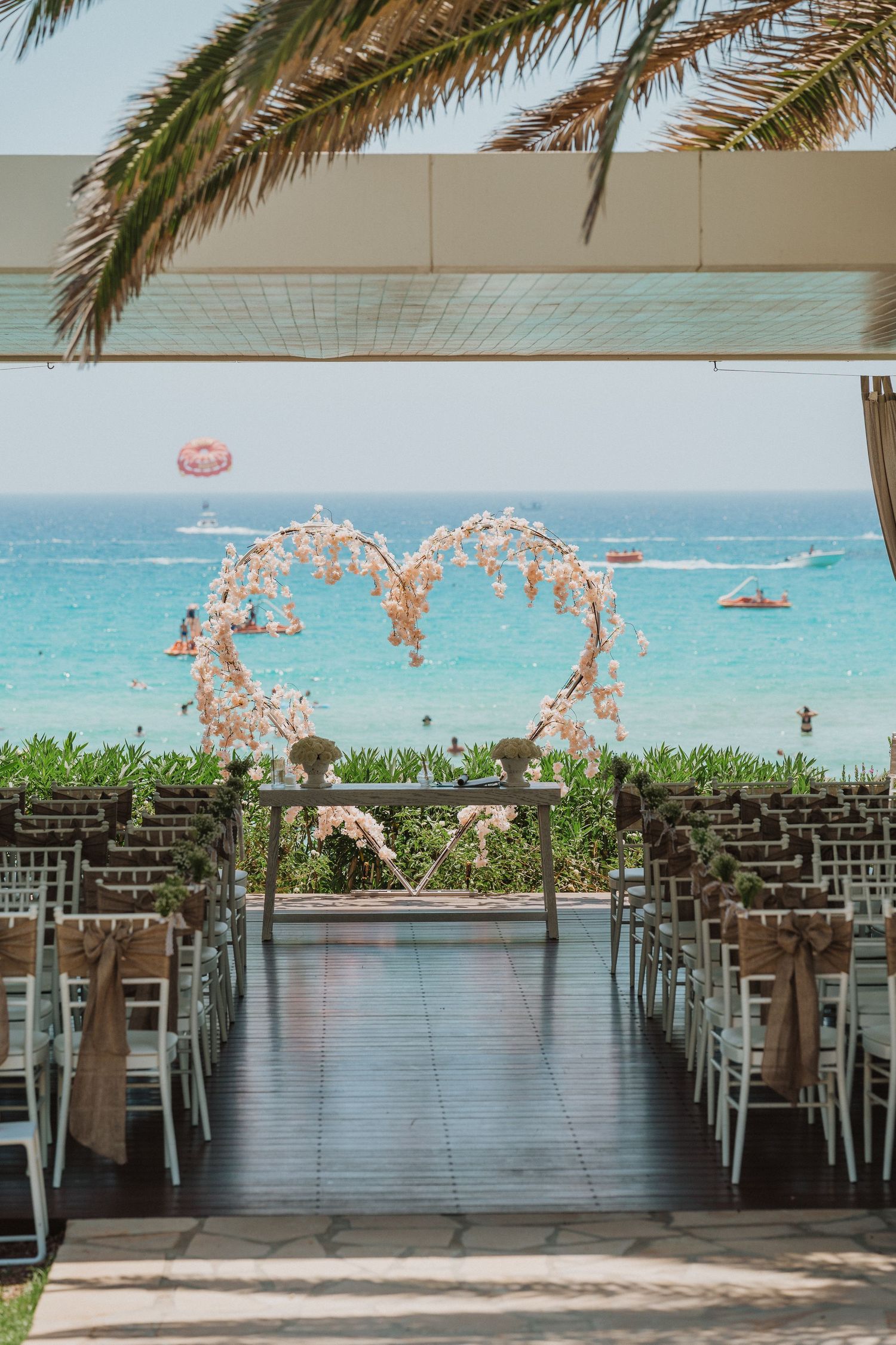 Beachfront wedding venue with heart-shaped floral arch and rows of chairs facing the ocean.