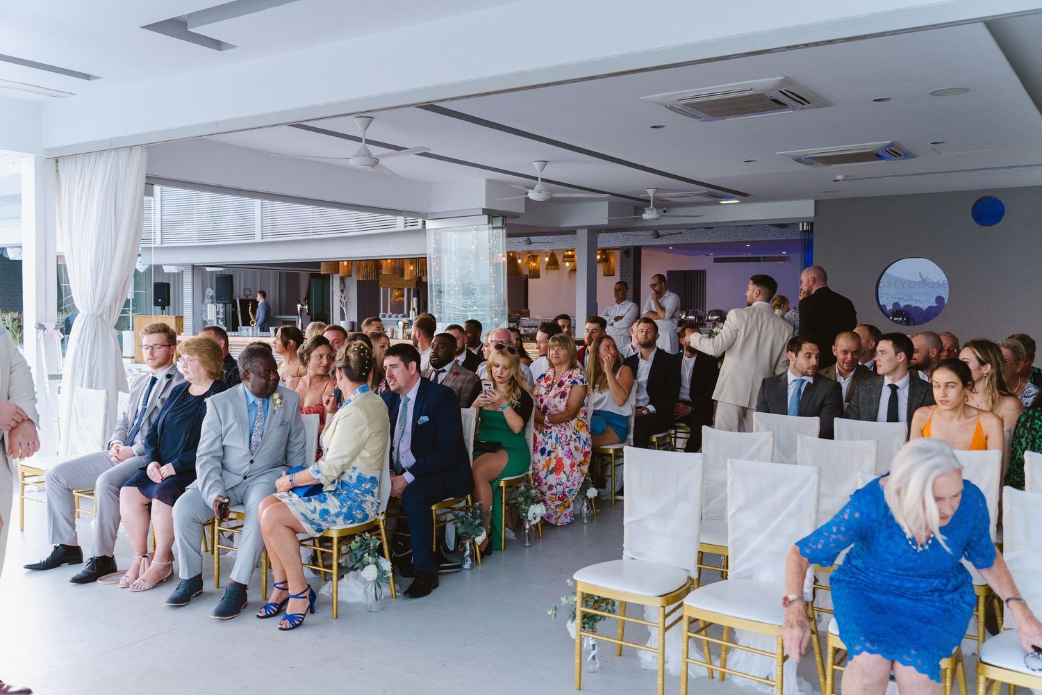 Wedding ceremony attendees gathered in a modern indoor venue with white decor.