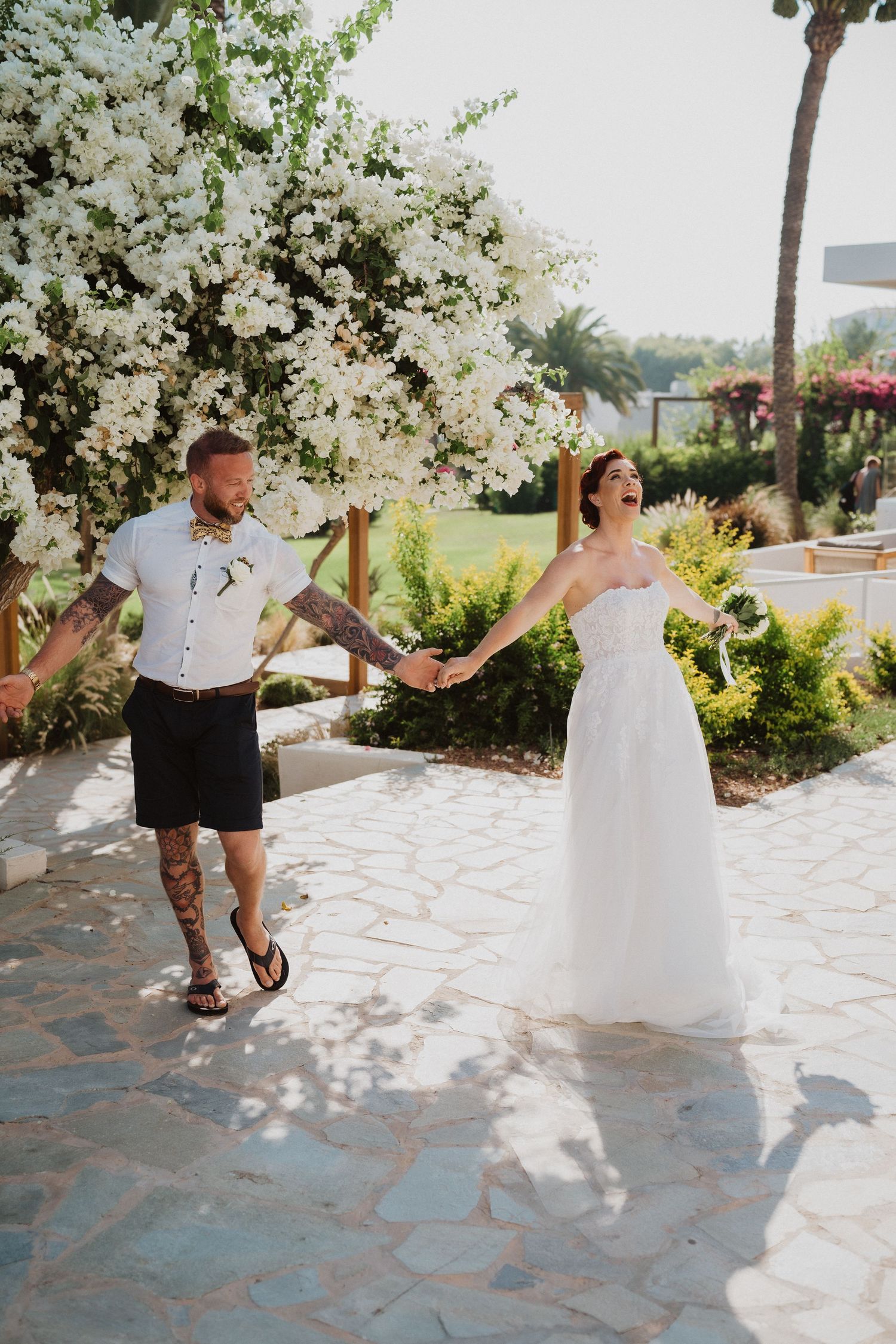 A couple celebrates with playful dance moves on a stone pathway during their destination wedding.