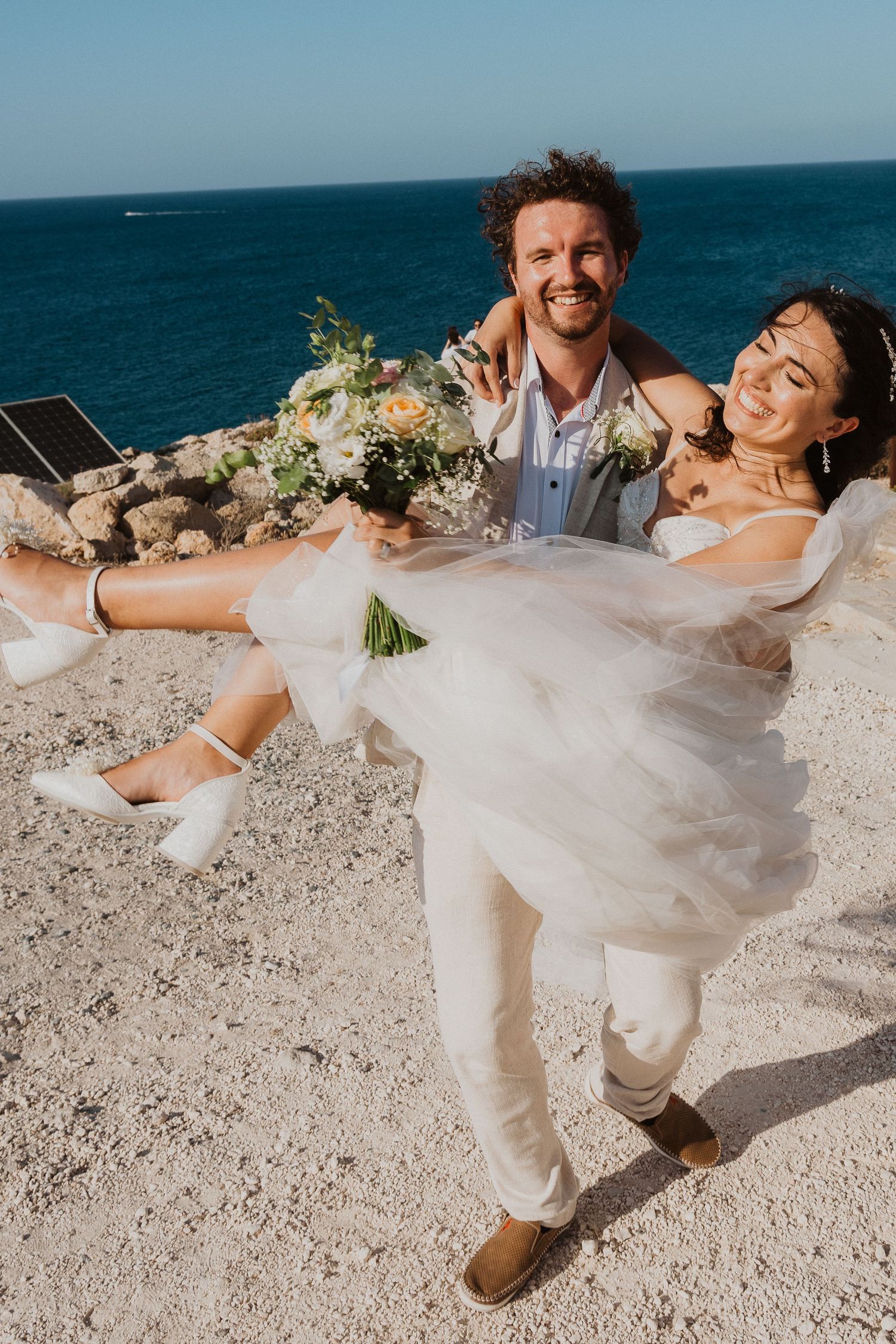 A celebratory moment as a groom lifts his bride on a scenic coastal overlook.
