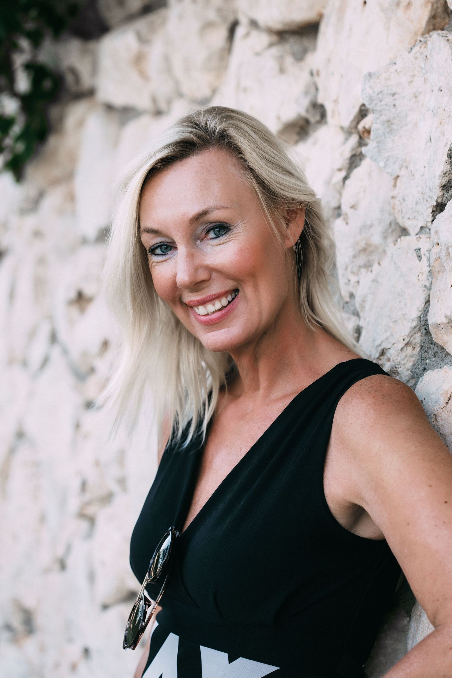 Woman in black sleeveless top poses against white stone wall.