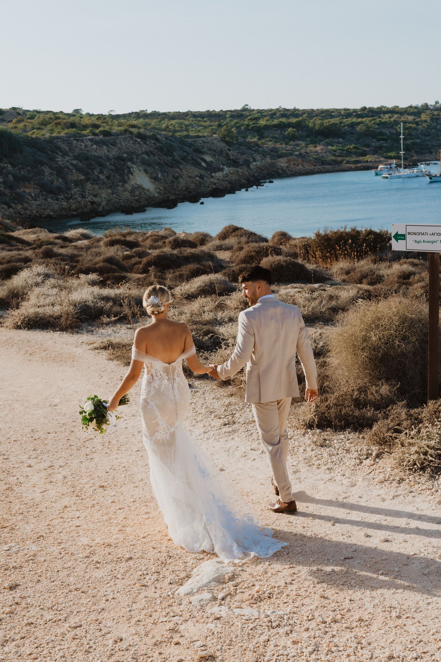 Newlyweds strolling together on a rocky coastal path with ocean views.