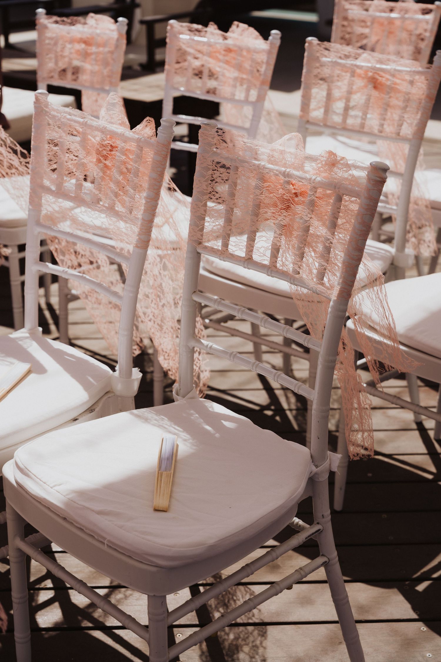 White chiavari chairs with peach lace sashes arranged for wedding ceremony.