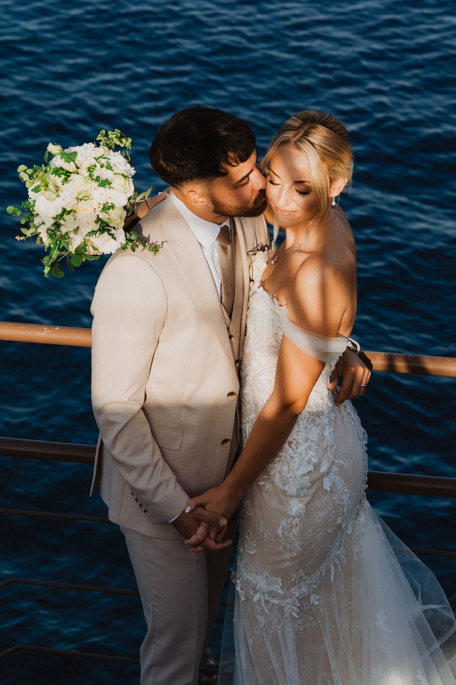 Intimate wedding portrait against deep blue Mediterranean waters at golden hour.