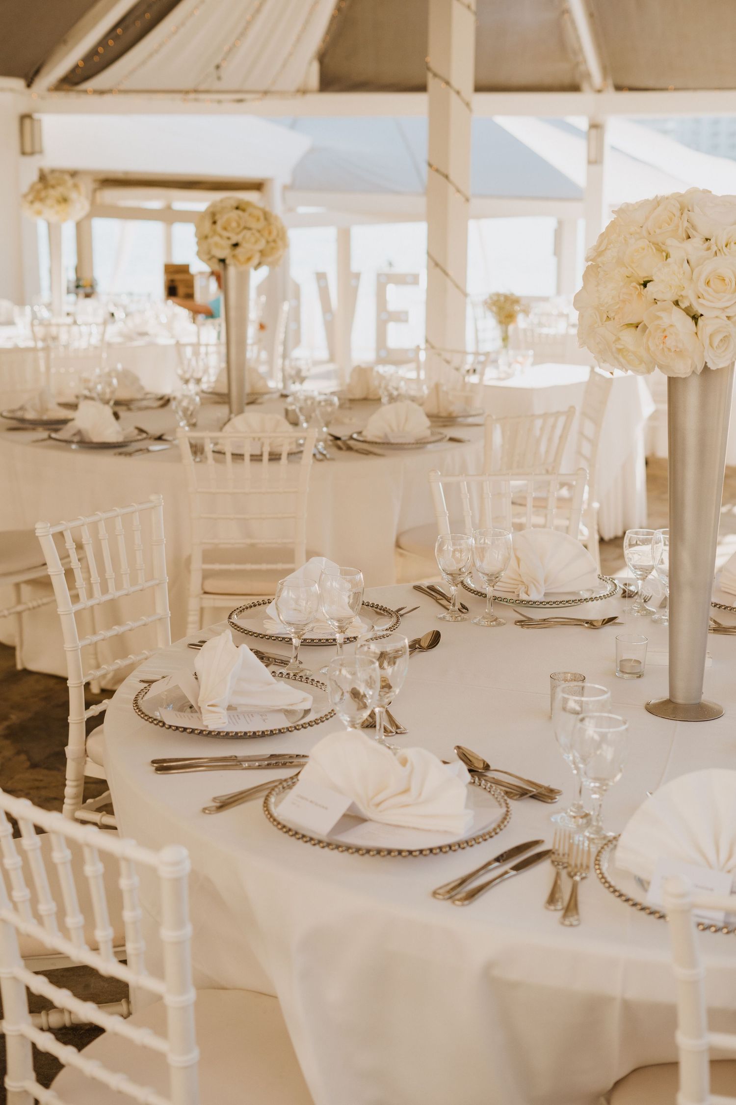 All-white wedding reception setup with Chiavari chairs and elegant table settings in a bright venue.