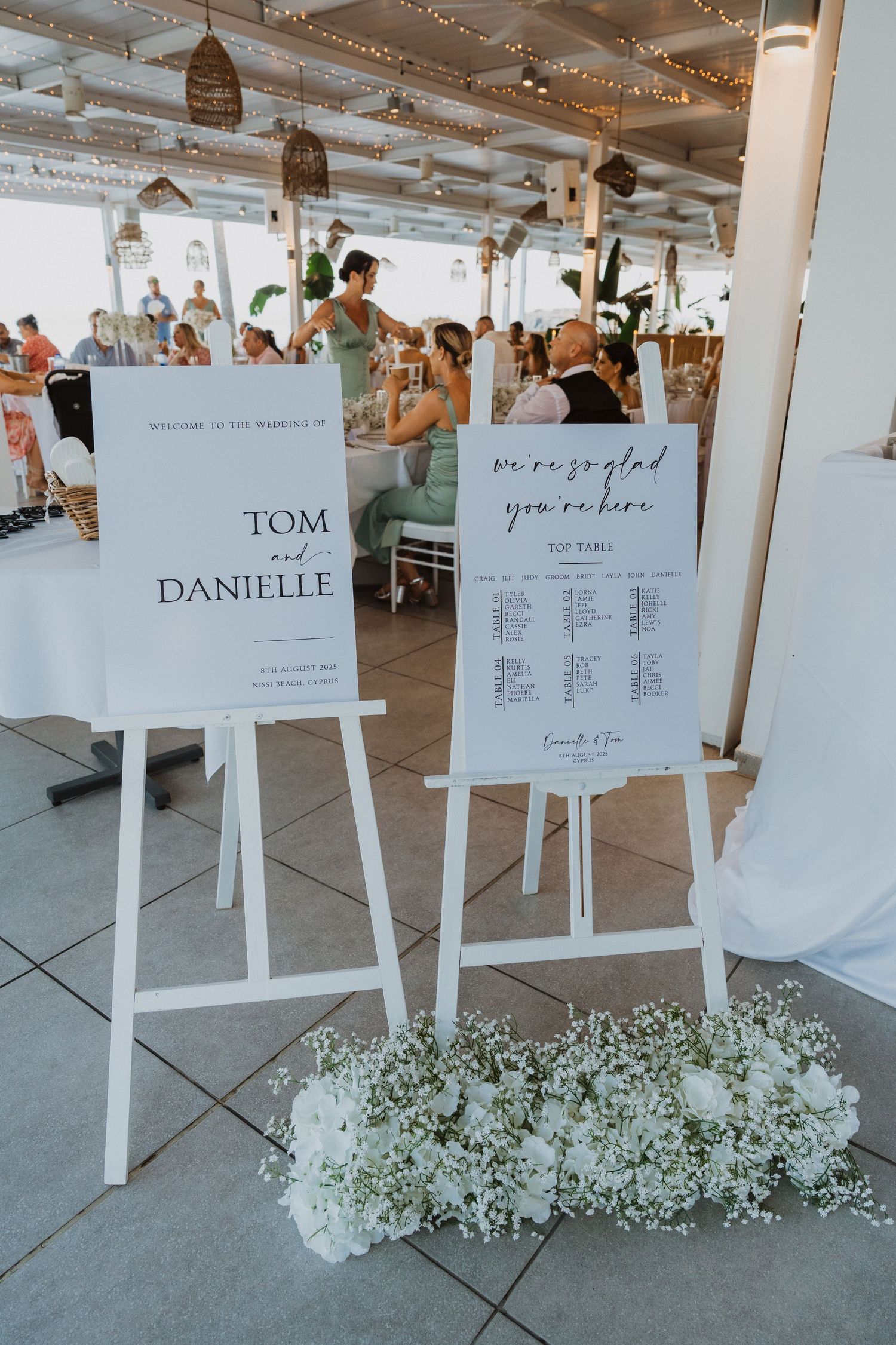 Modern wedding seating charts arranged on white easels with floral decorations.