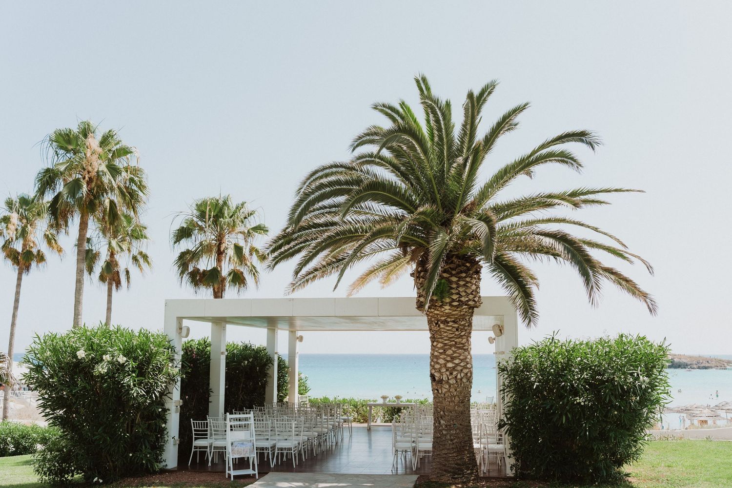 White gazebo nestled between palm trees overlooking a tropical beach with calm ocean waters.