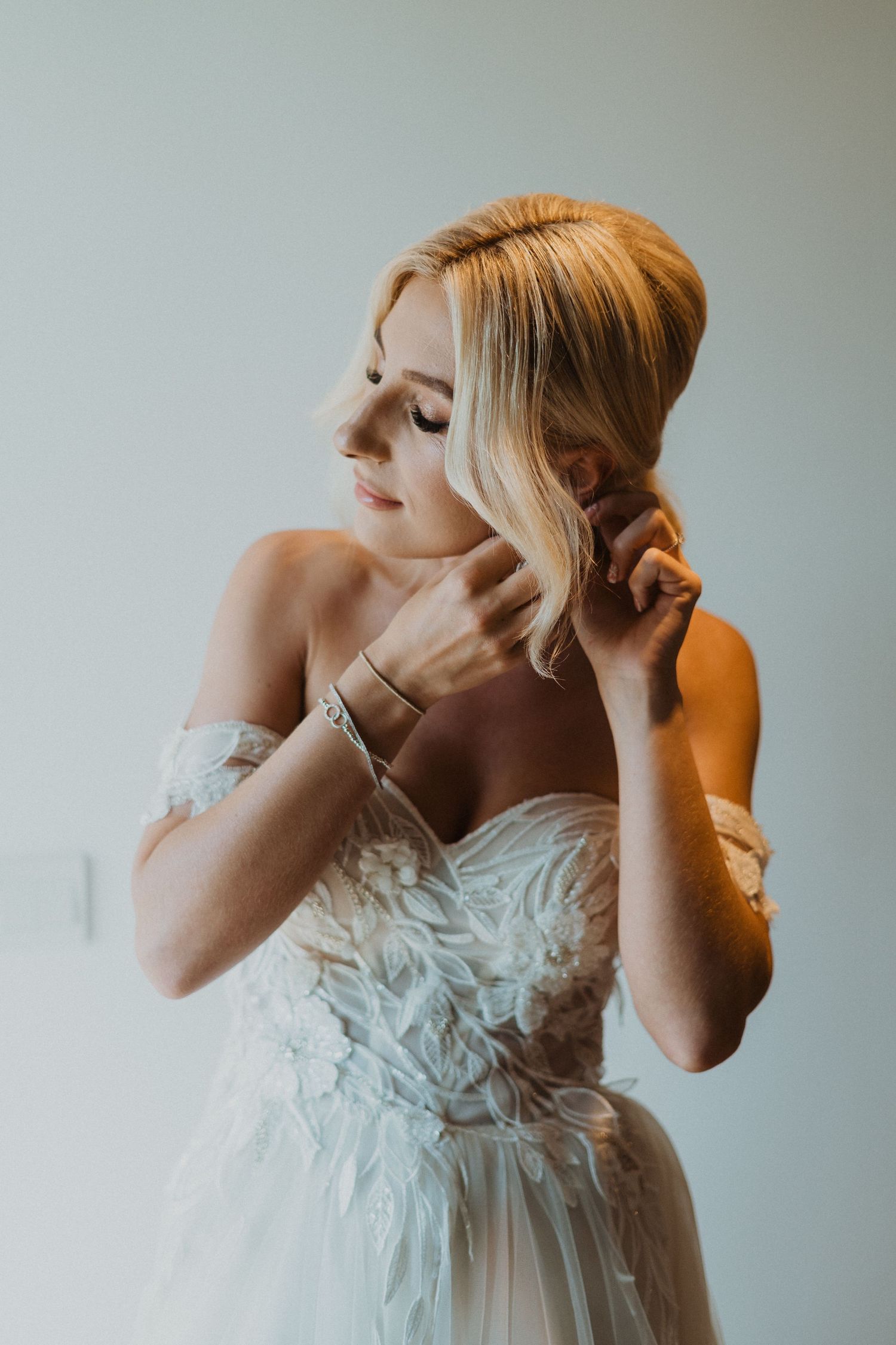 Side profile of bride adjusting jewelry while wearing a feathered wedding gown.