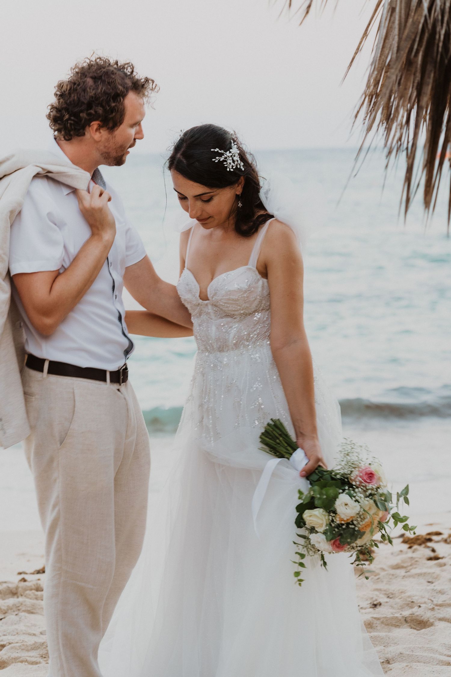 Elegant beach wedding photo showing couple in light summer attire against ocean backdrop.