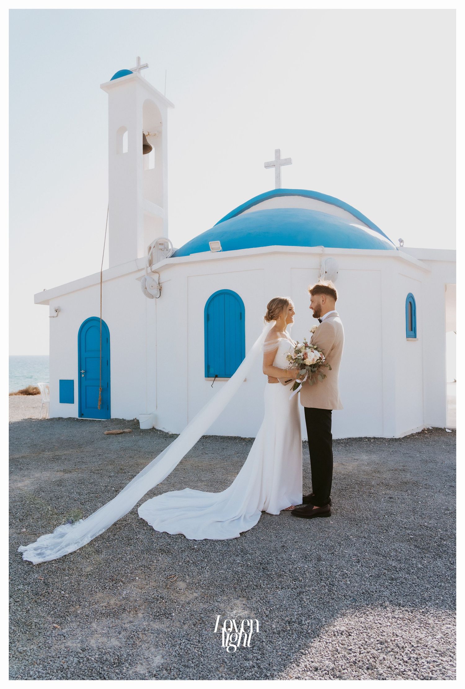 Elegant wedding portrait in front of a pristine white Mediterranean church with blue dome.