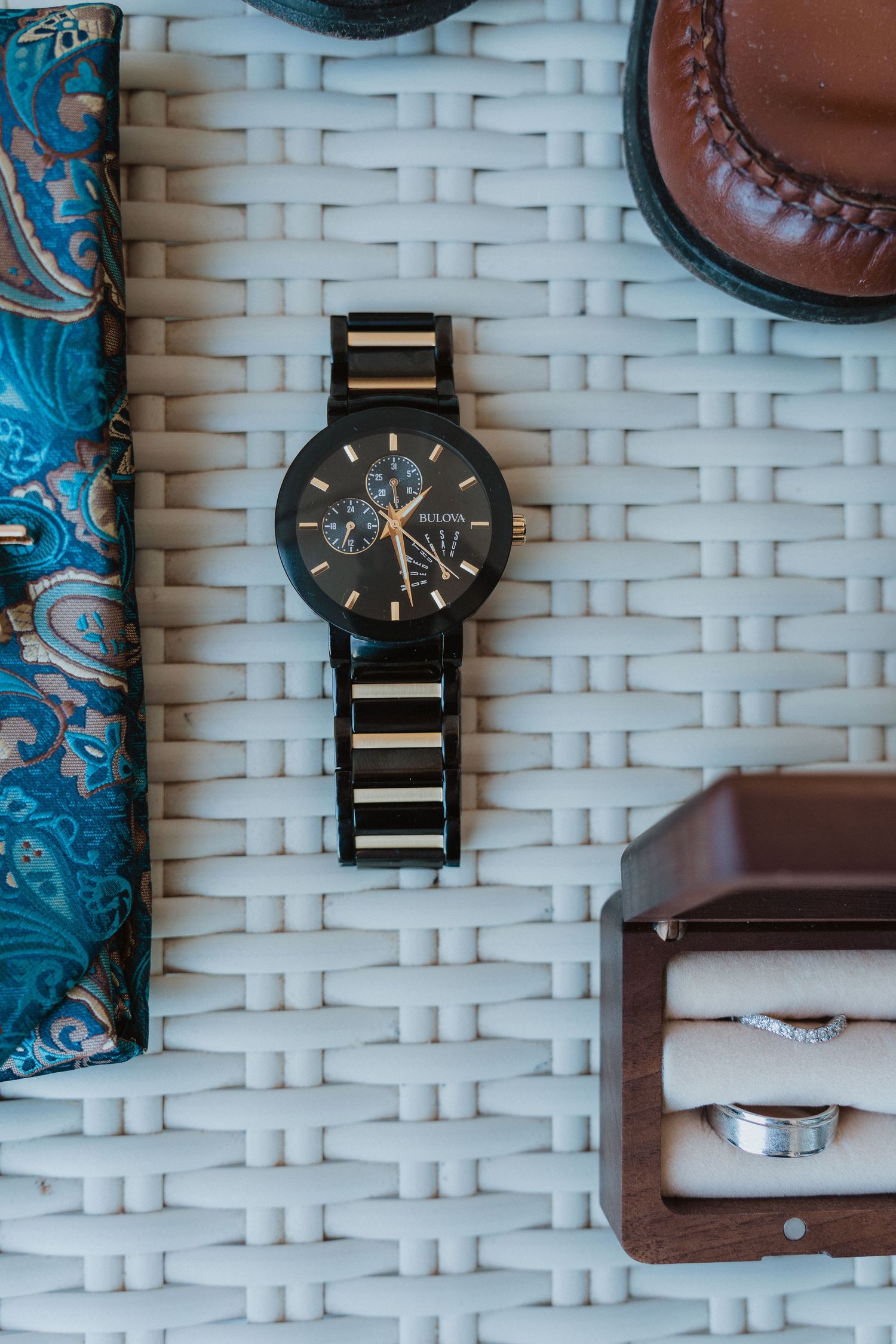 Black and gold wristwatch displayed on white woven surface alongside leather accessories and blue fabric.