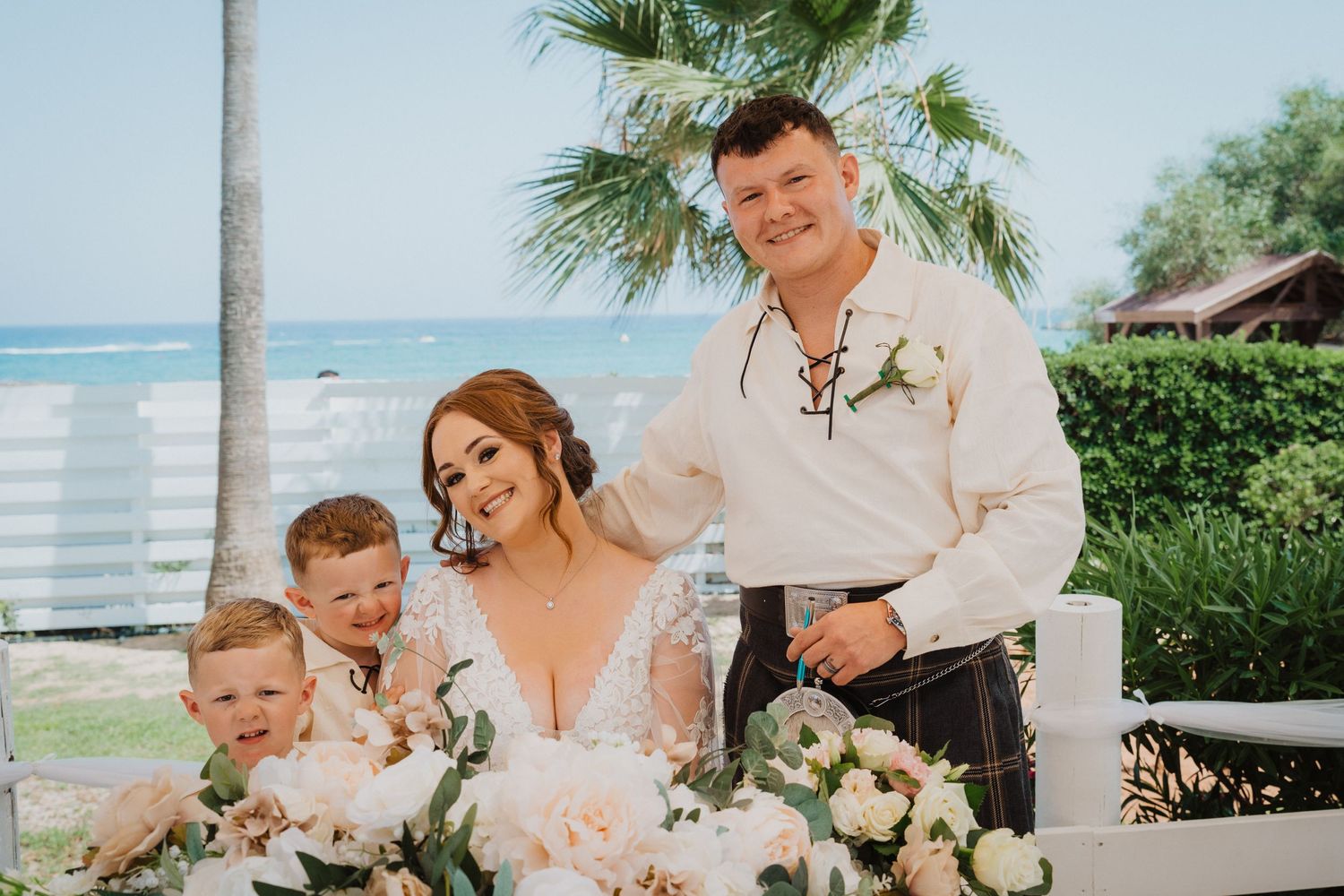 Beachfront wedding portrait featuring traditional Scottish attire and elegant floral arrangements.