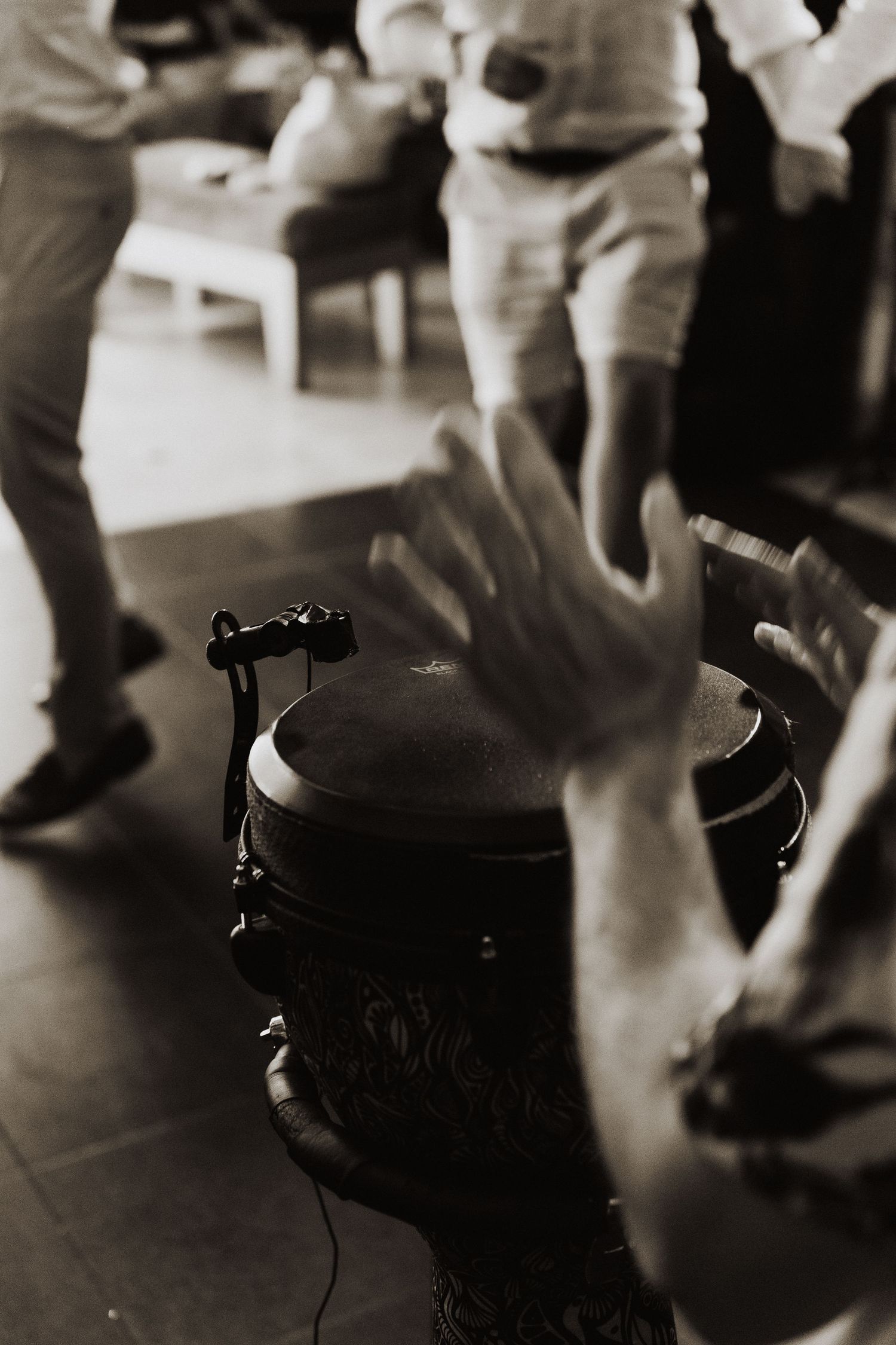 Black and white photo of hands and dancing feet around a drum during a lively musical performance.