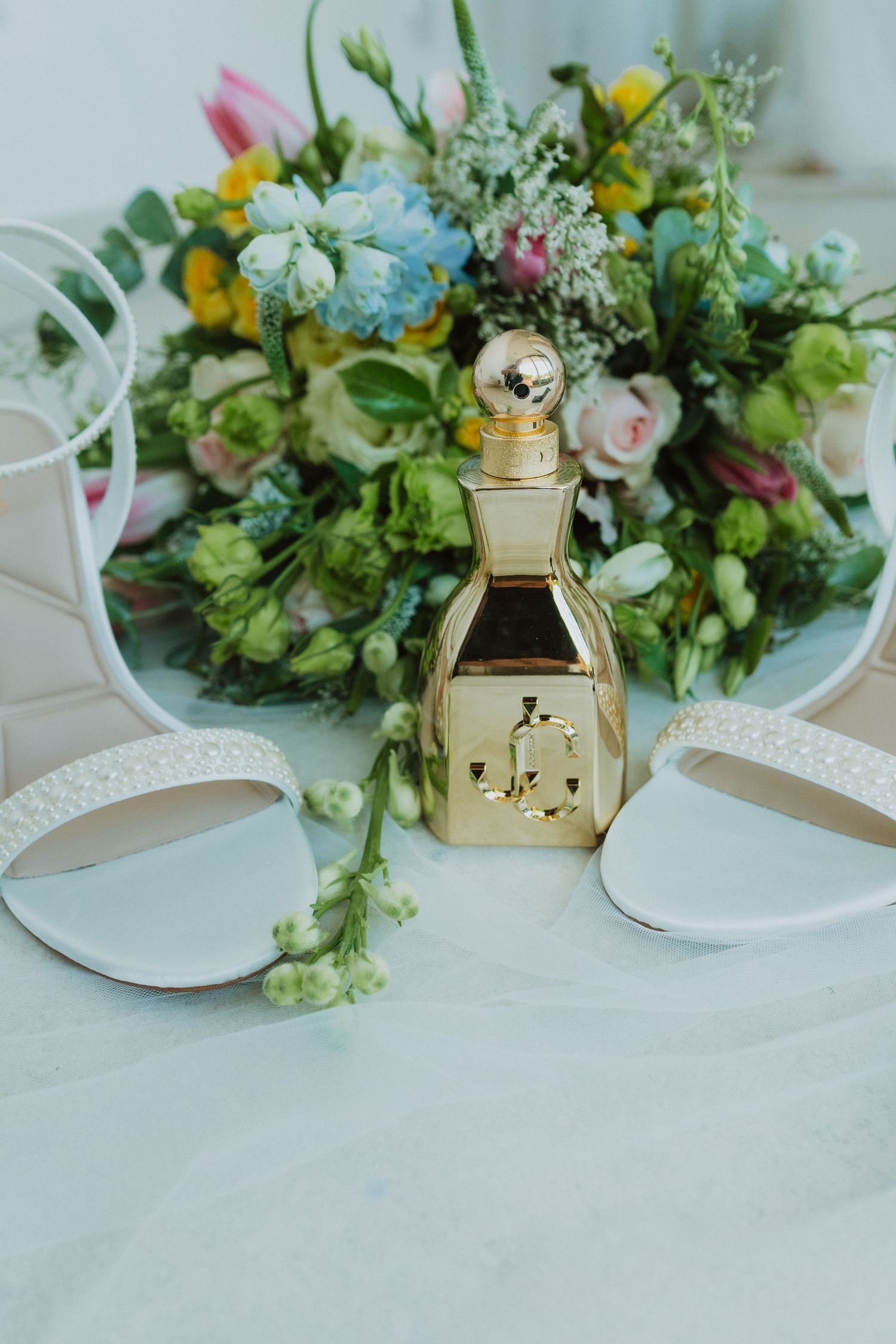 Elegant floral table decor with fresh spring blooms and gold accents arranged on a white tablecloth for a wedding reception.