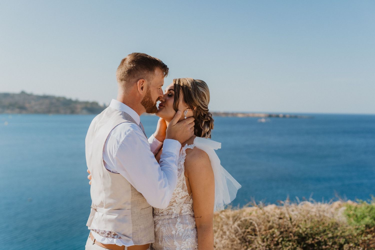 Wedding couple poses against blue ocean view on sunny day.