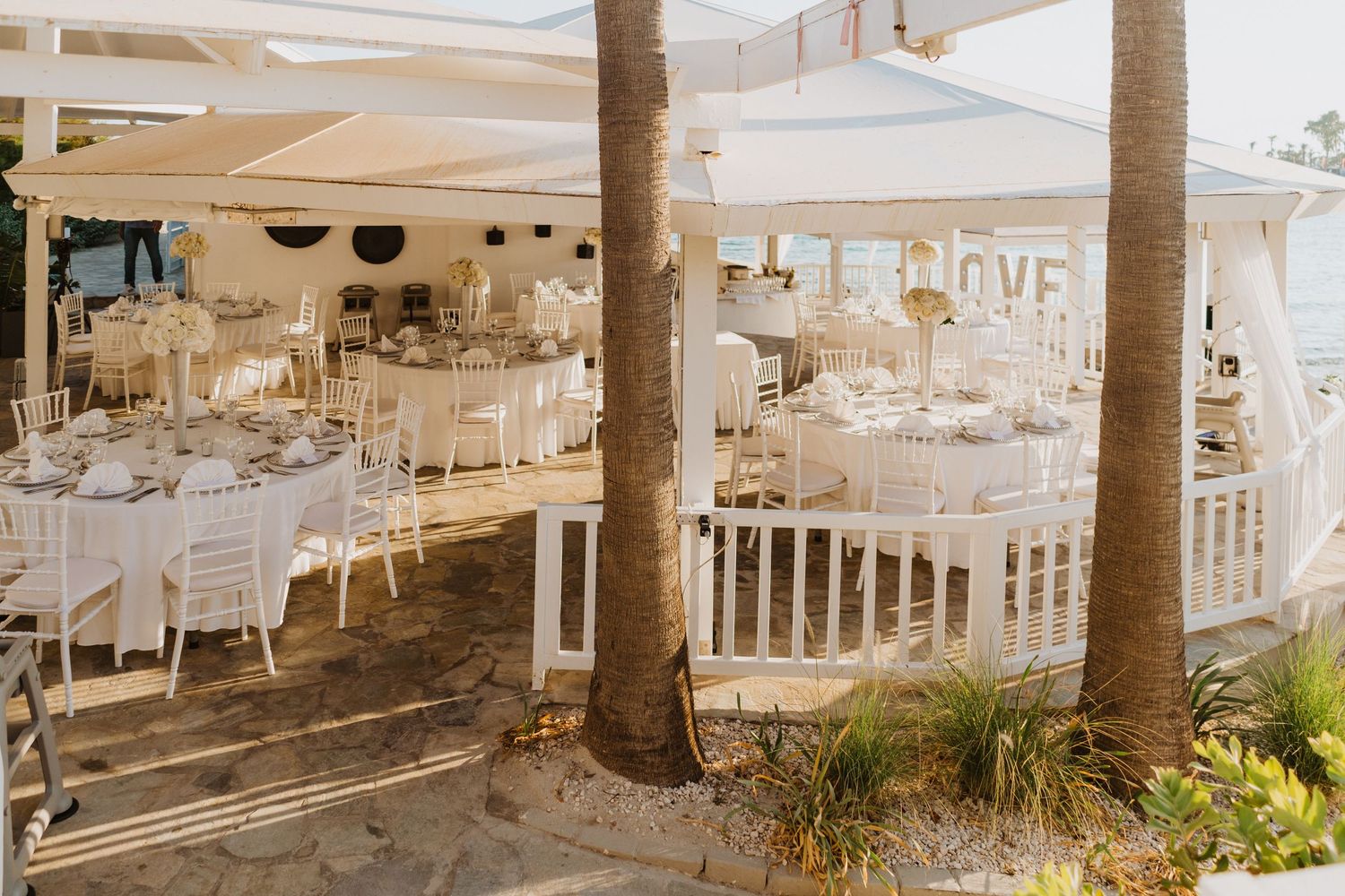 Outdoor wedding venue setup with white canopies and palm trees creating a tropical atmosphere.