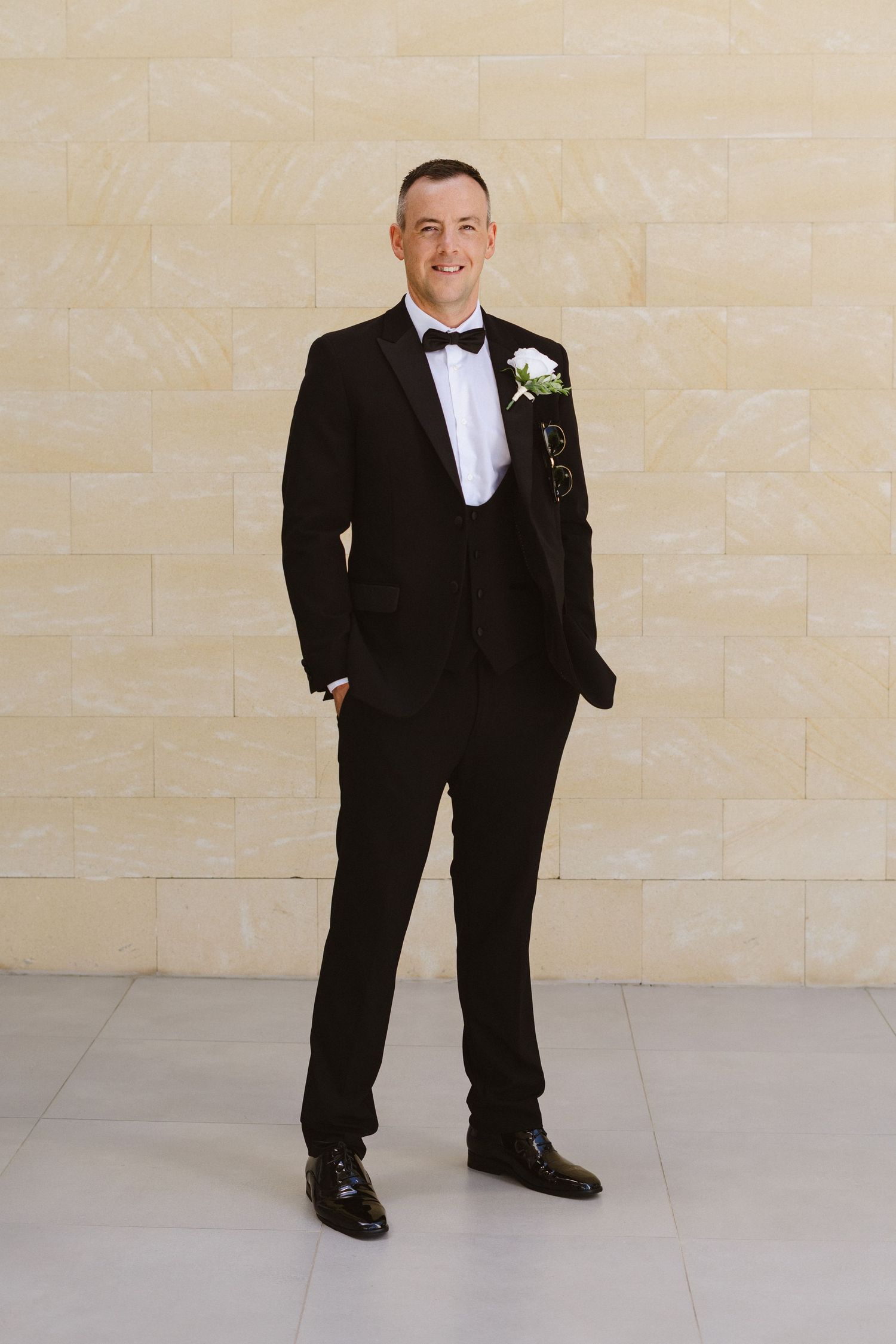 Groom in classic black tuxedo and boutonniere poses for formal wedding portraits.