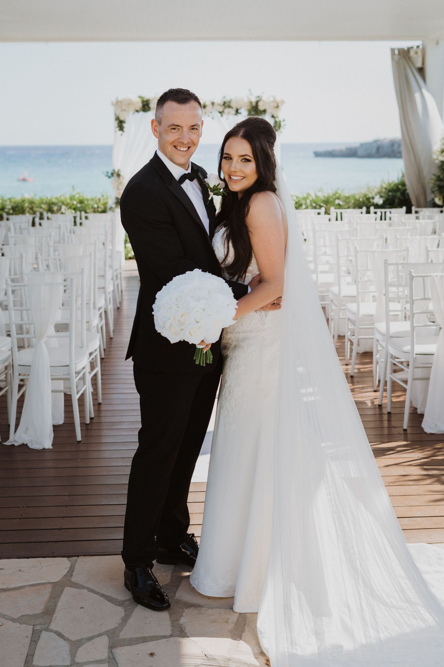 Couple sharing tender moment at beachfront ceremony site with white chairs.