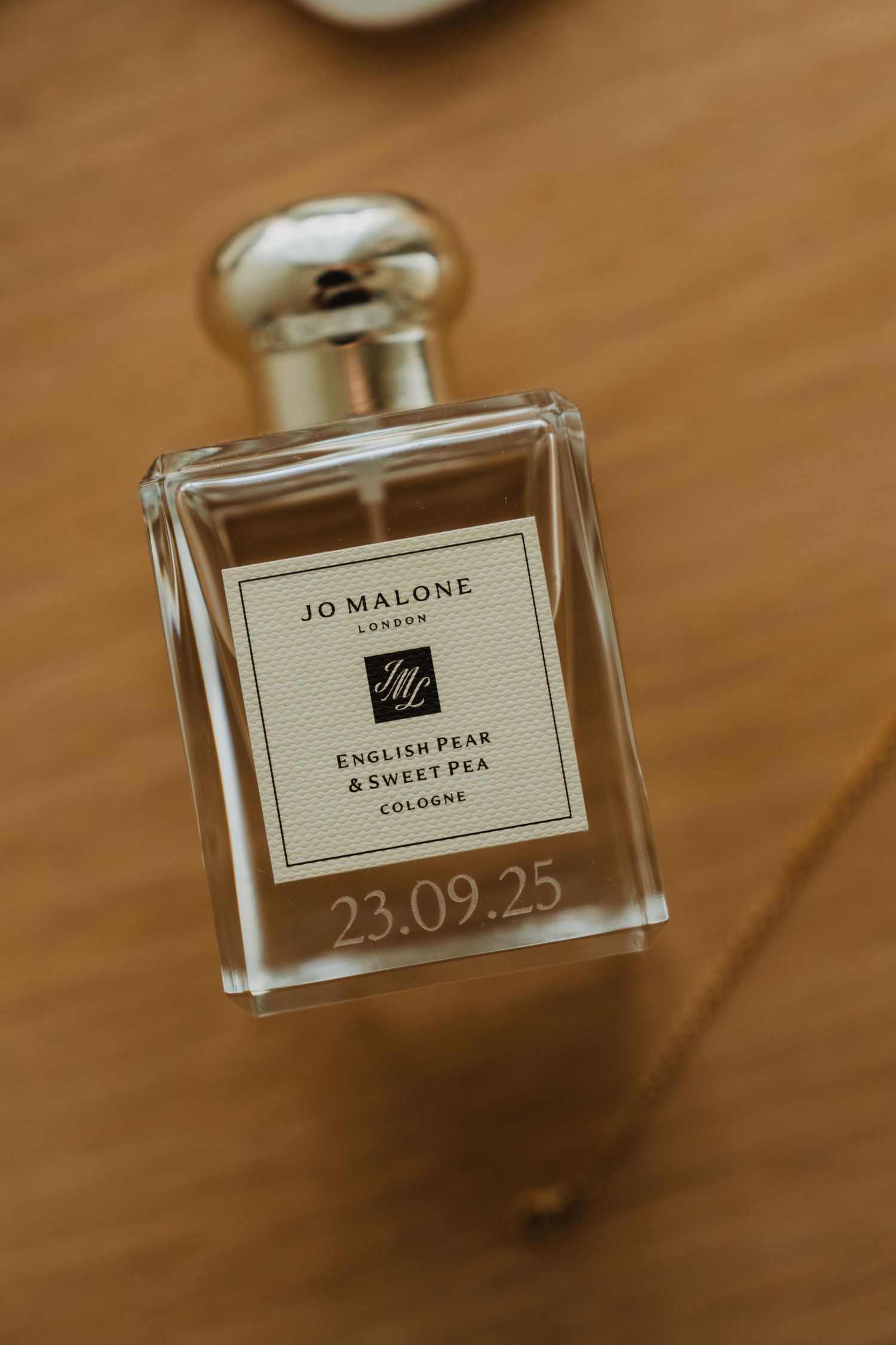 A Jo Malone perfume bottle with custom wedding date engraving displayed on wooden surface.
