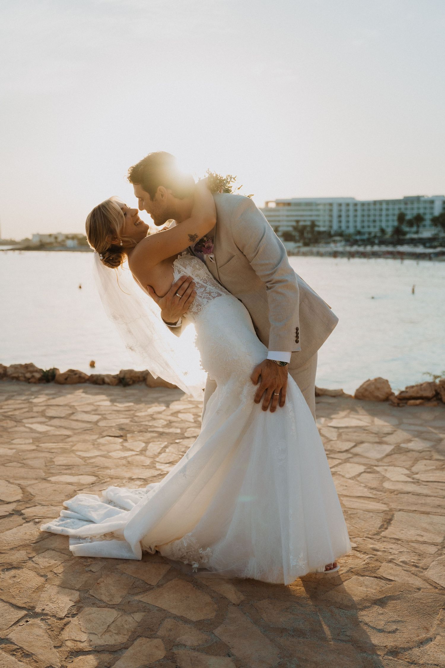 Romantic dip kiss between newlyweds on stone terrace overlooking the ocean.