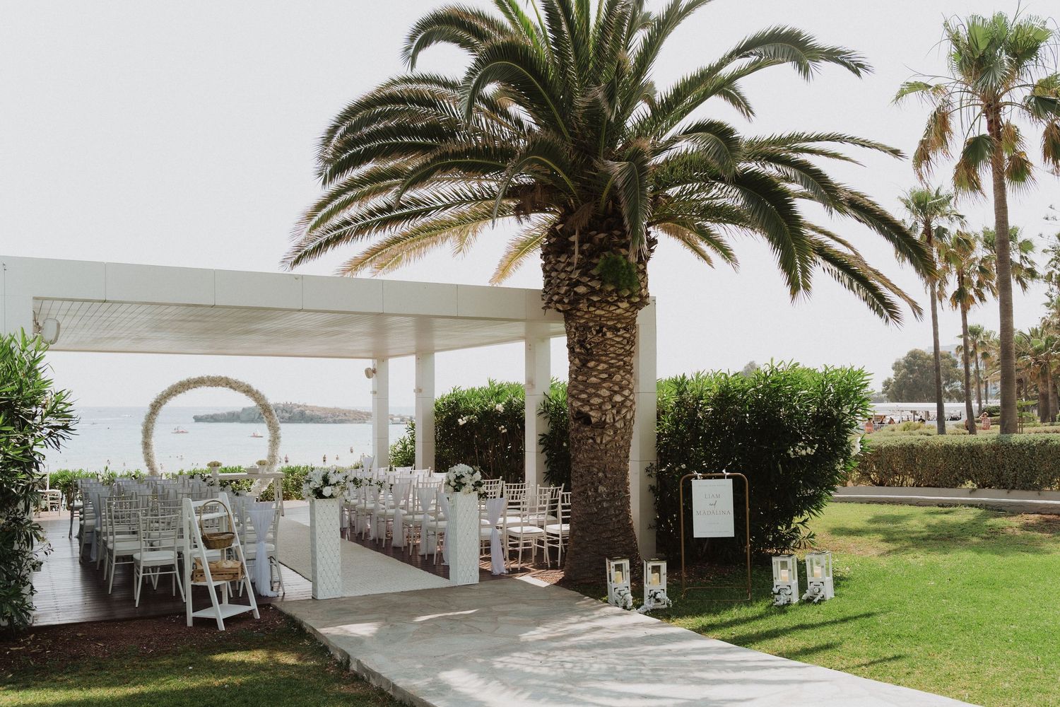 Outdoor beach wedding venue with white chairs and palm tree backdrop.