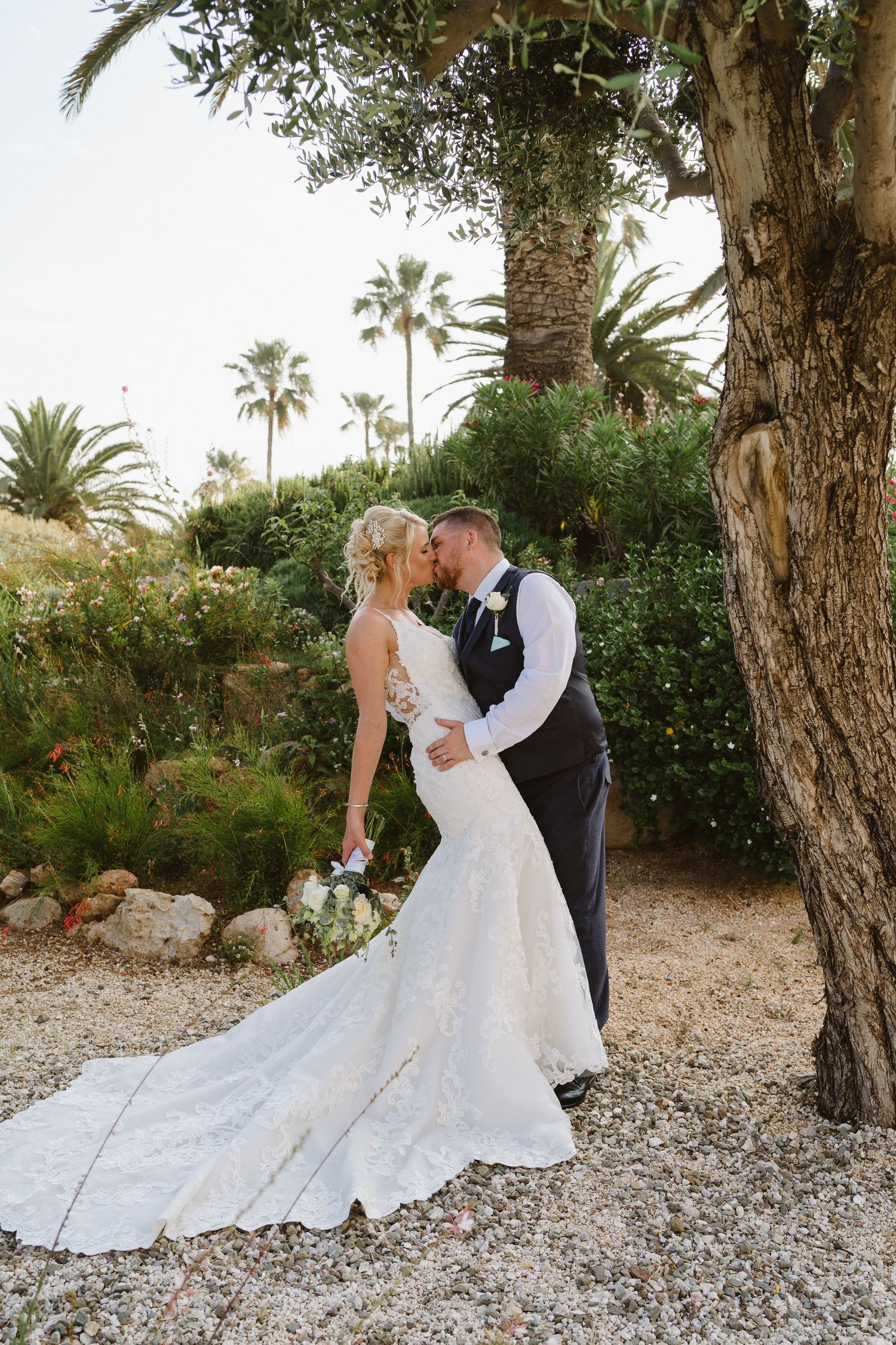 Elegant garden wedding portrait among palm trees with bride's flowing lace train.