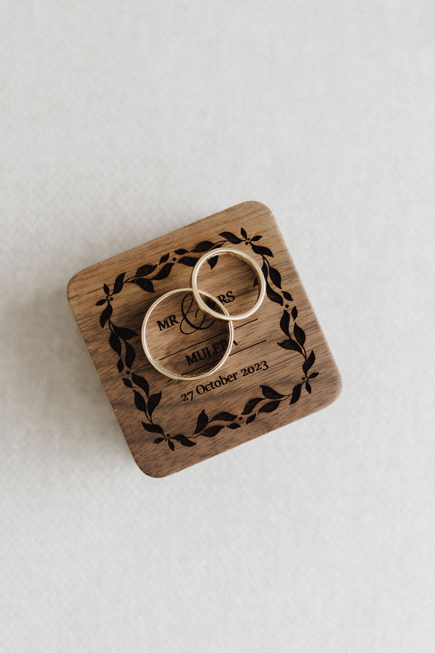Two wedding rings displayed in a wooden box with engraved floral design.