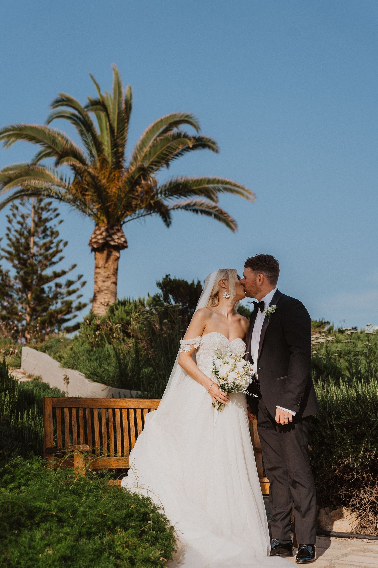 A romantic wedding portrait under palm trees in a beautiful Mediterranean garden setting.