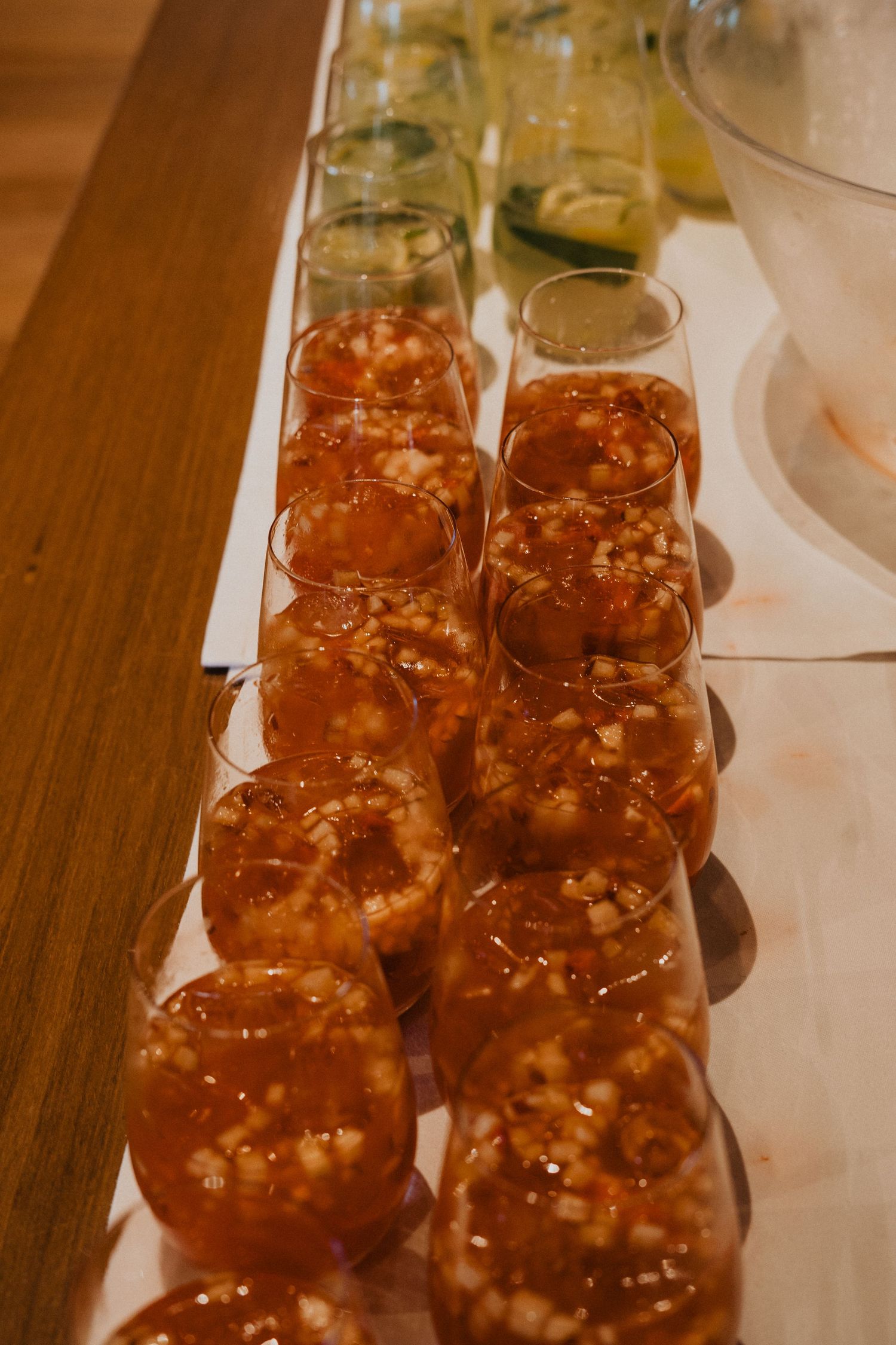 Row of amber-colored cocktails lined up on a wooden surface at an event.