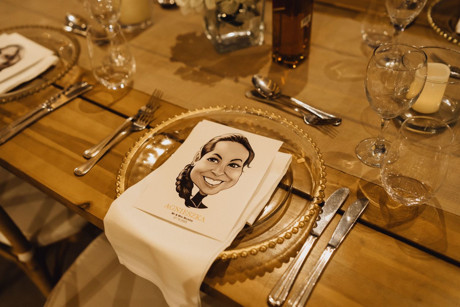 A formal place setting at a wedding reception with a custom napkin portrait and gold charger plate.