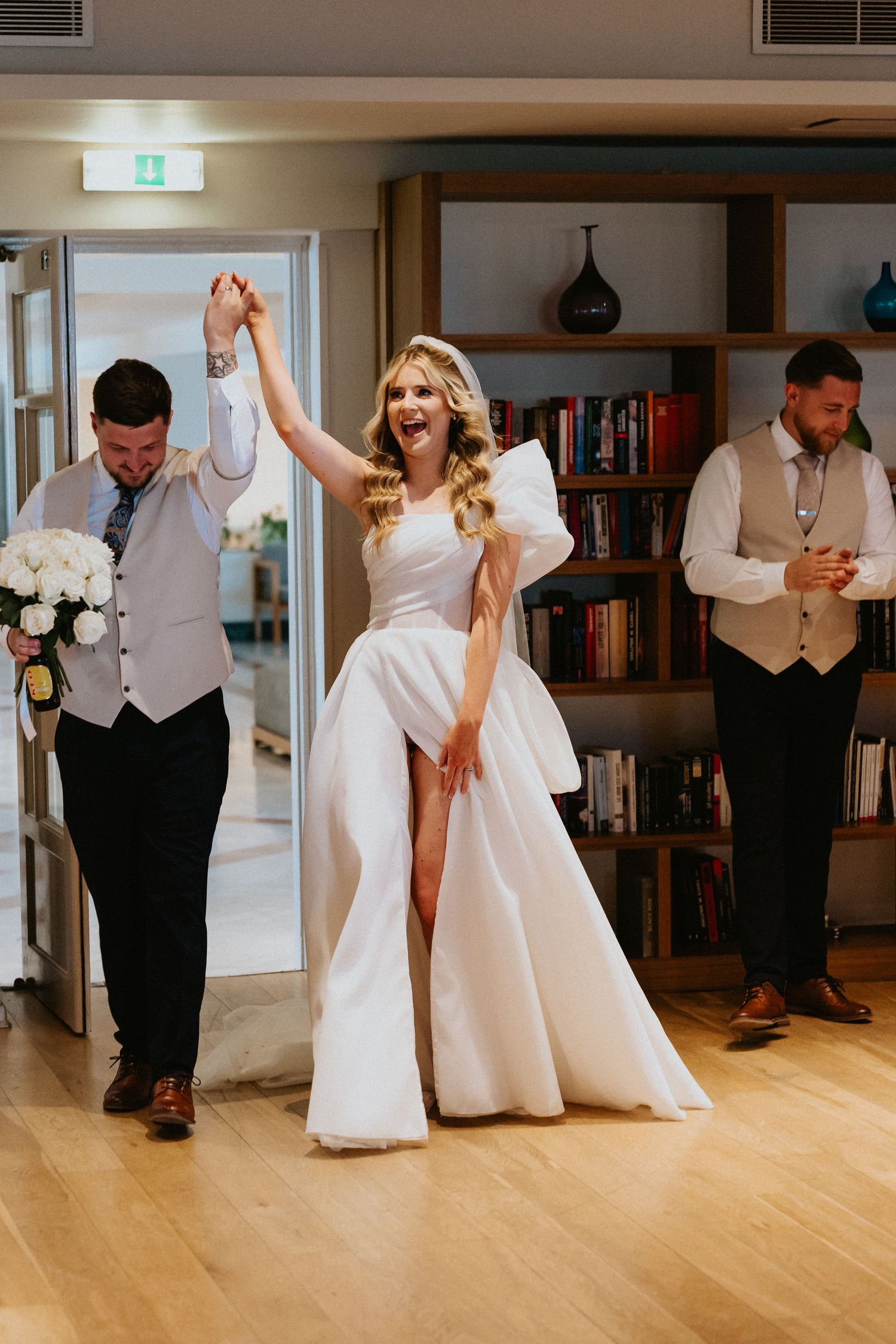 Joyful celebration moment as newlyweds dance in library-themed reception space.