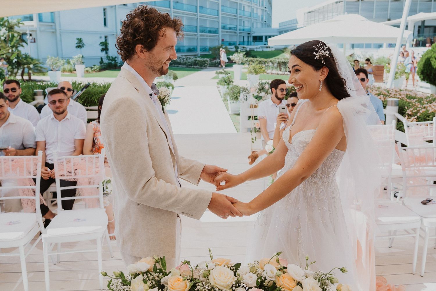 Sweet moment during ring exchange at outdoor wedding with beige and white decor.