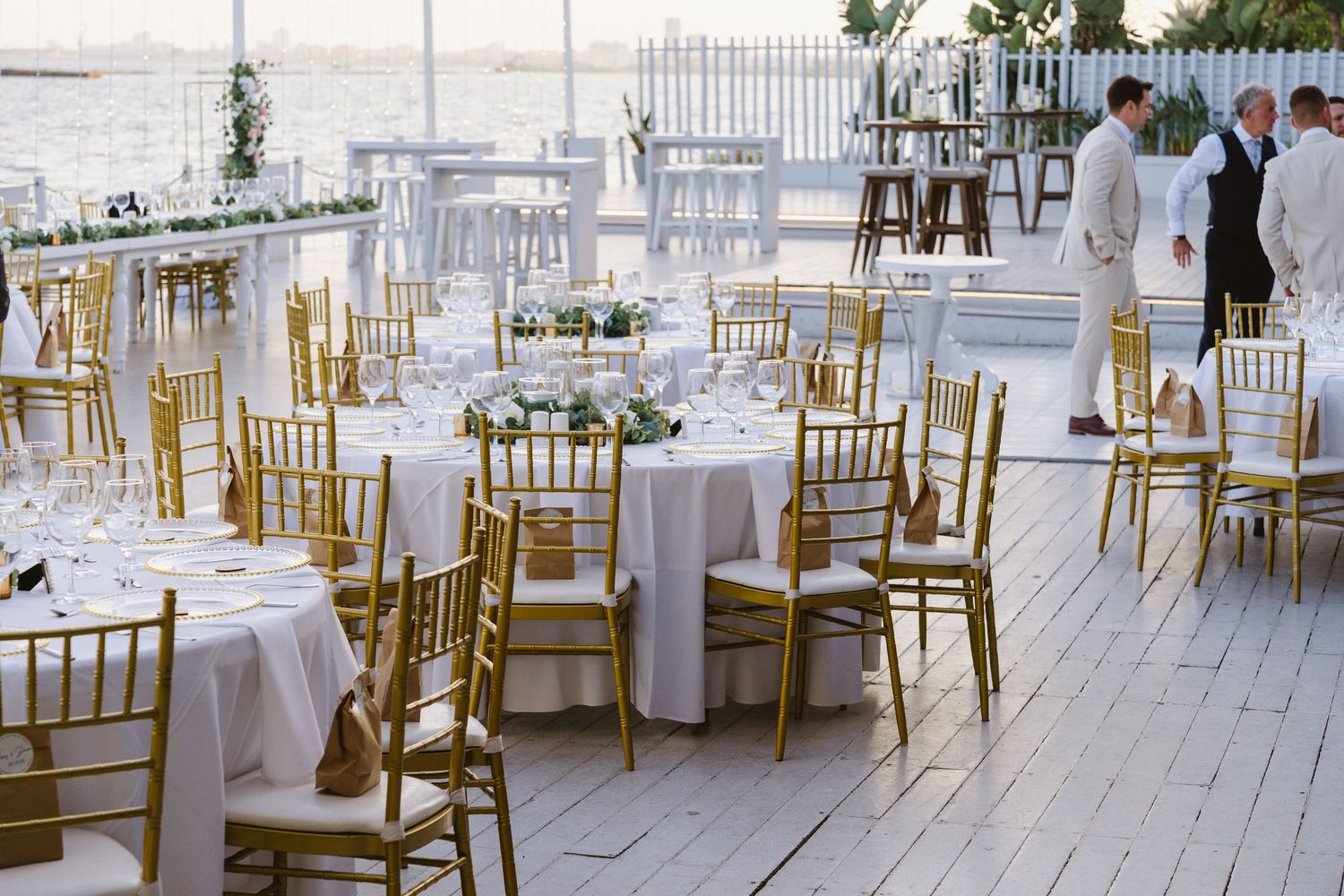 Outdoor waterfront wedding reception setup with gold chiavari chairs and round tables.