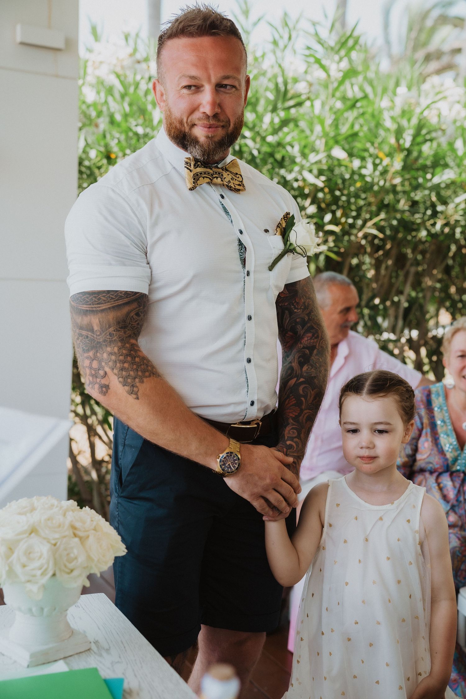 A formal wedding portrait in a lush garden setting with white floral decorations.