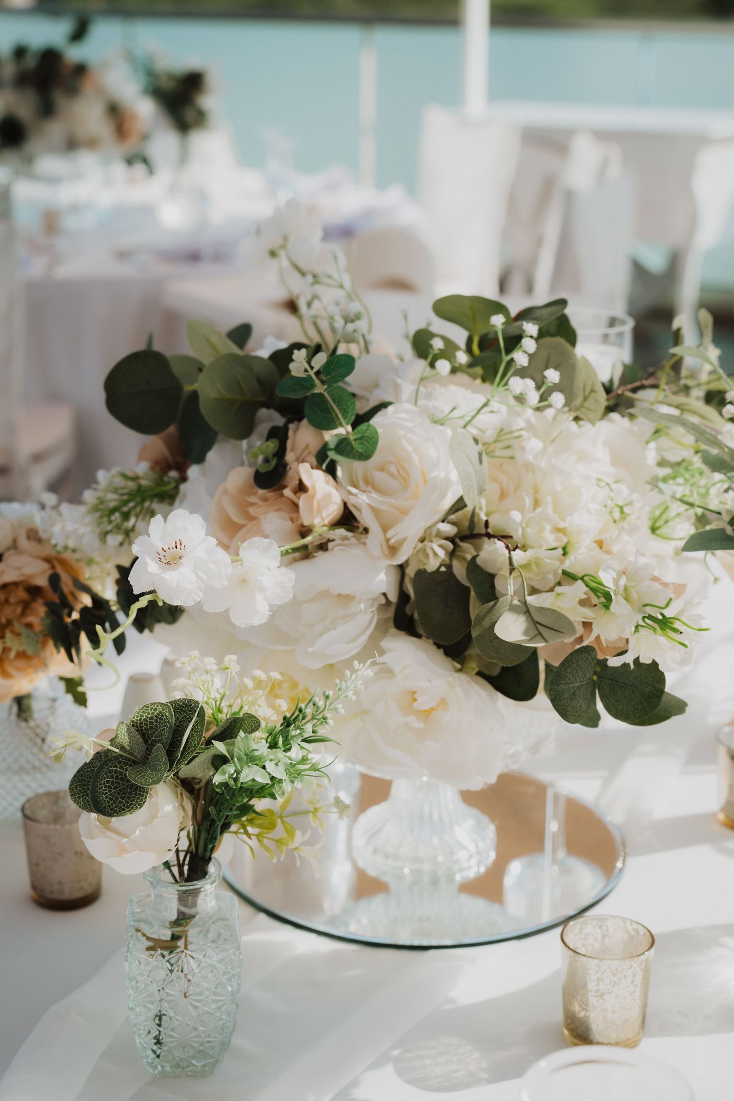 Elegant place setting with blush roses and eucalyptus centerpiece on white tablecloth.