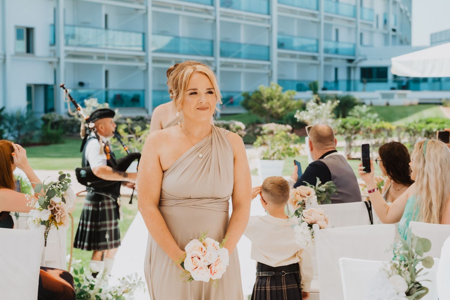 Wedding attendant walks down aisle with bagpiper playing in background.