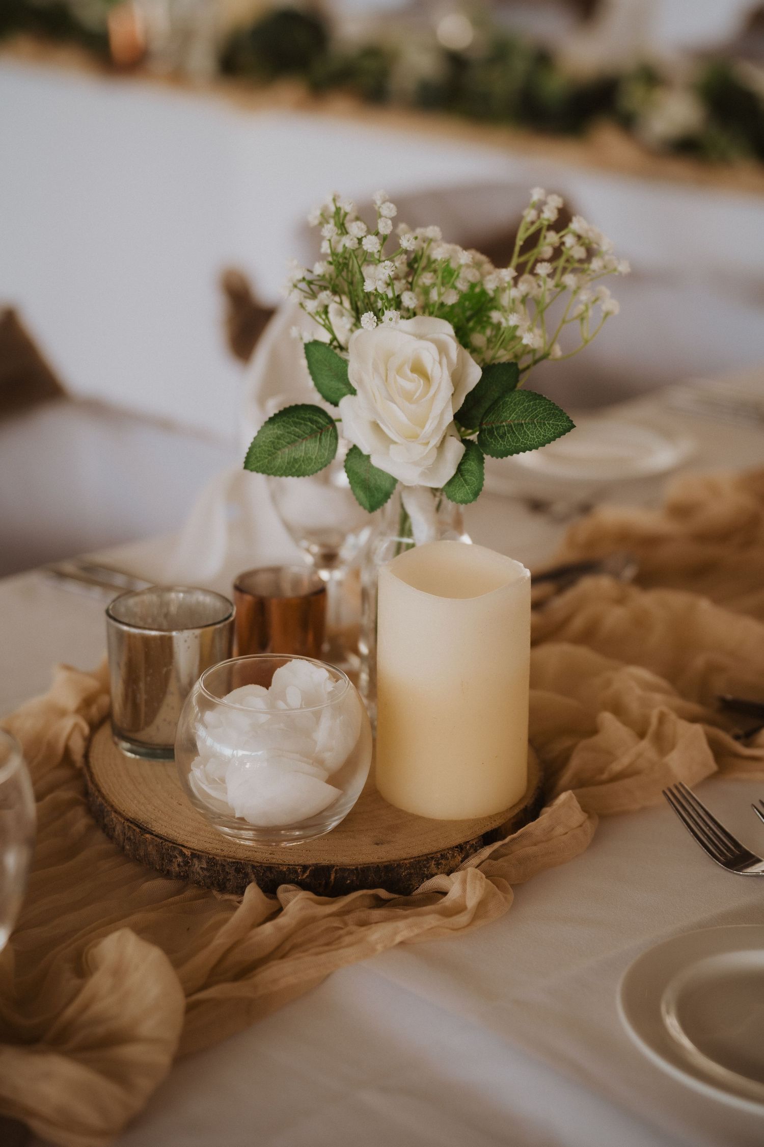 Elegant centerpiece with white rose, baby's breath, and candle on wooden slice charger.
