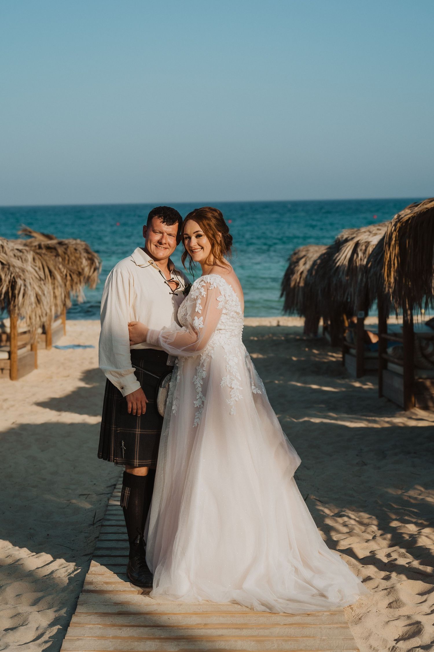 Romantic beach wedding portrait with palm-thatched umbrellas in the background.