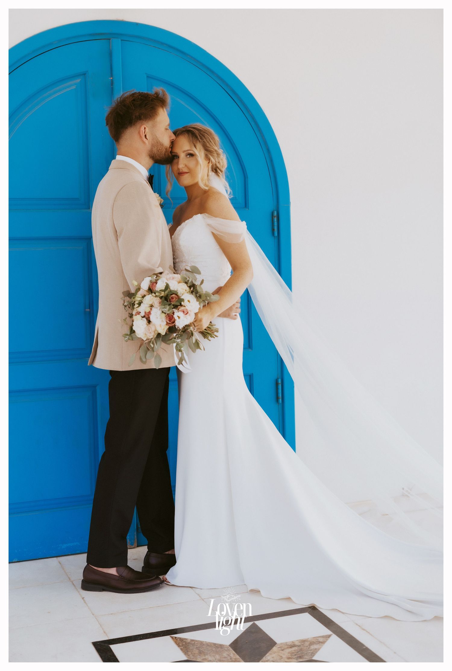 Elegant wedding portrait against vibrant blue door with bride holding pastel floral bouquet.