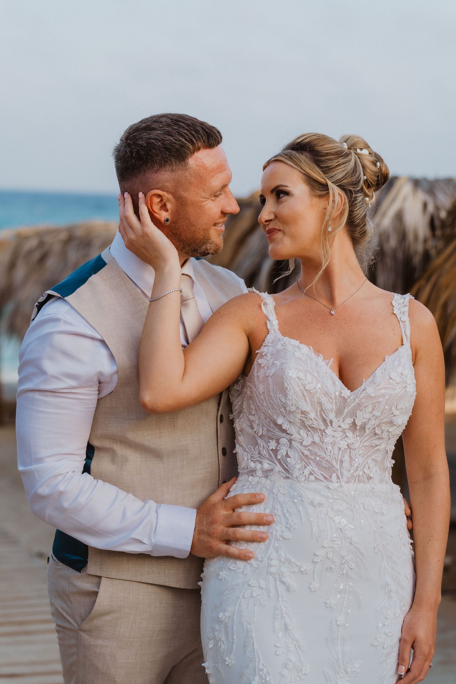 A couple in wedding attire shares intimate moments on a beach during sunset in a series of romantic poses.