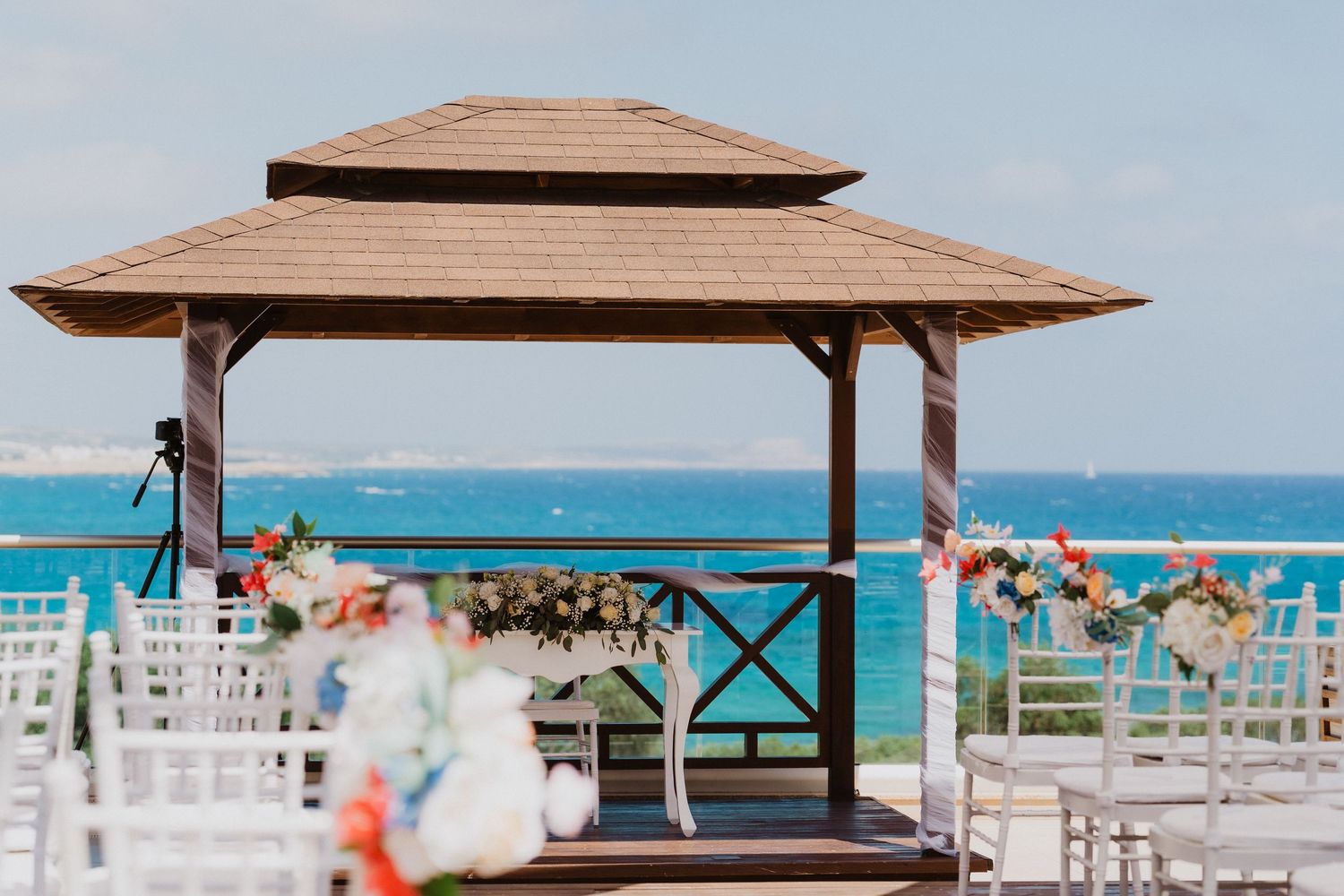Wooden umbrellas and white chairs line a pristine beach with turquoise waters and blue sky in the background.