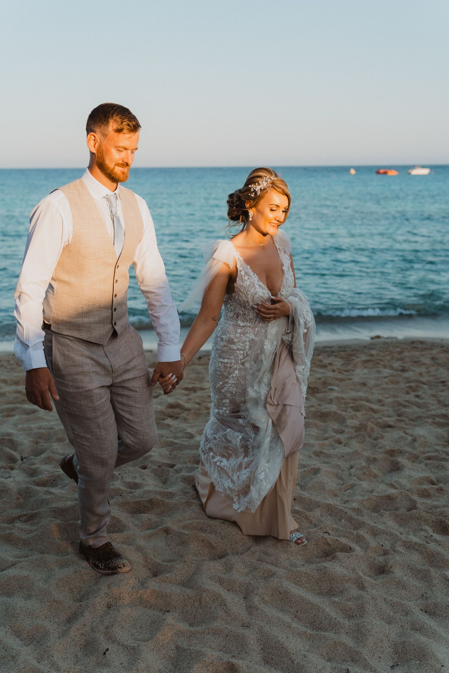 Wedding couple walks together on sandy beach during golden hour photoshoot.