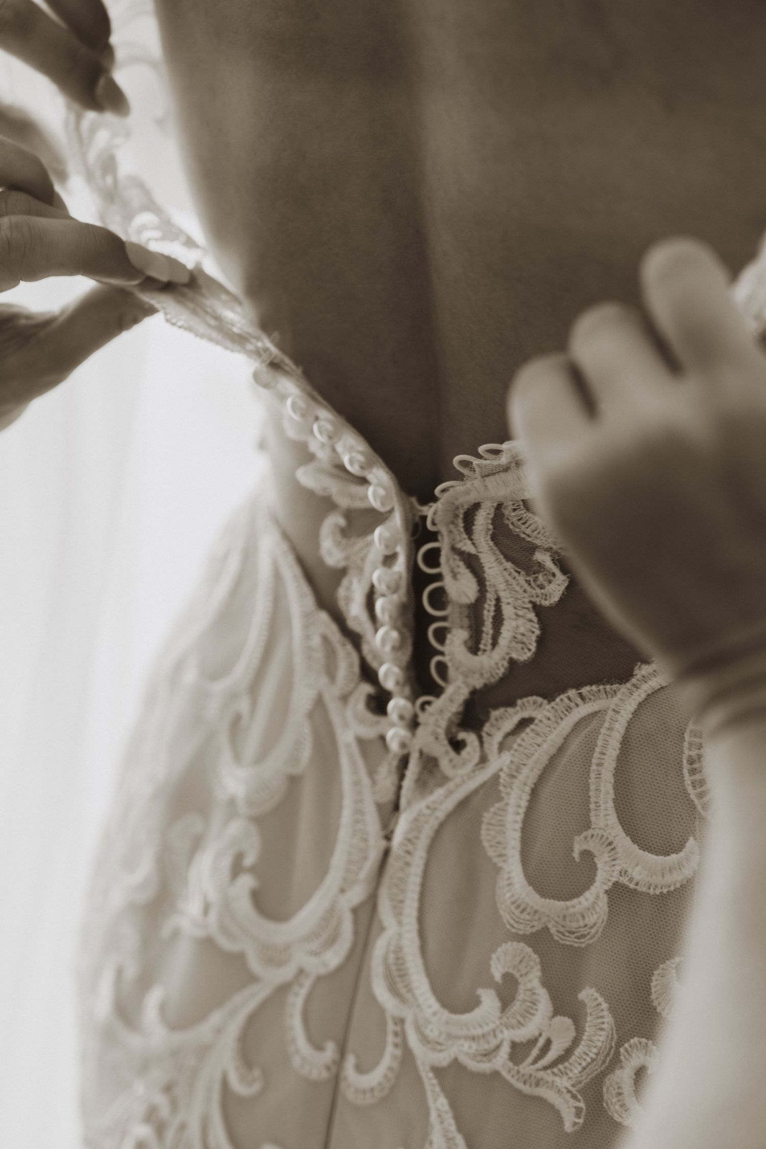 Delicate white lace trim detail on wedding dress fabric shown in sepia toned close-up photography.