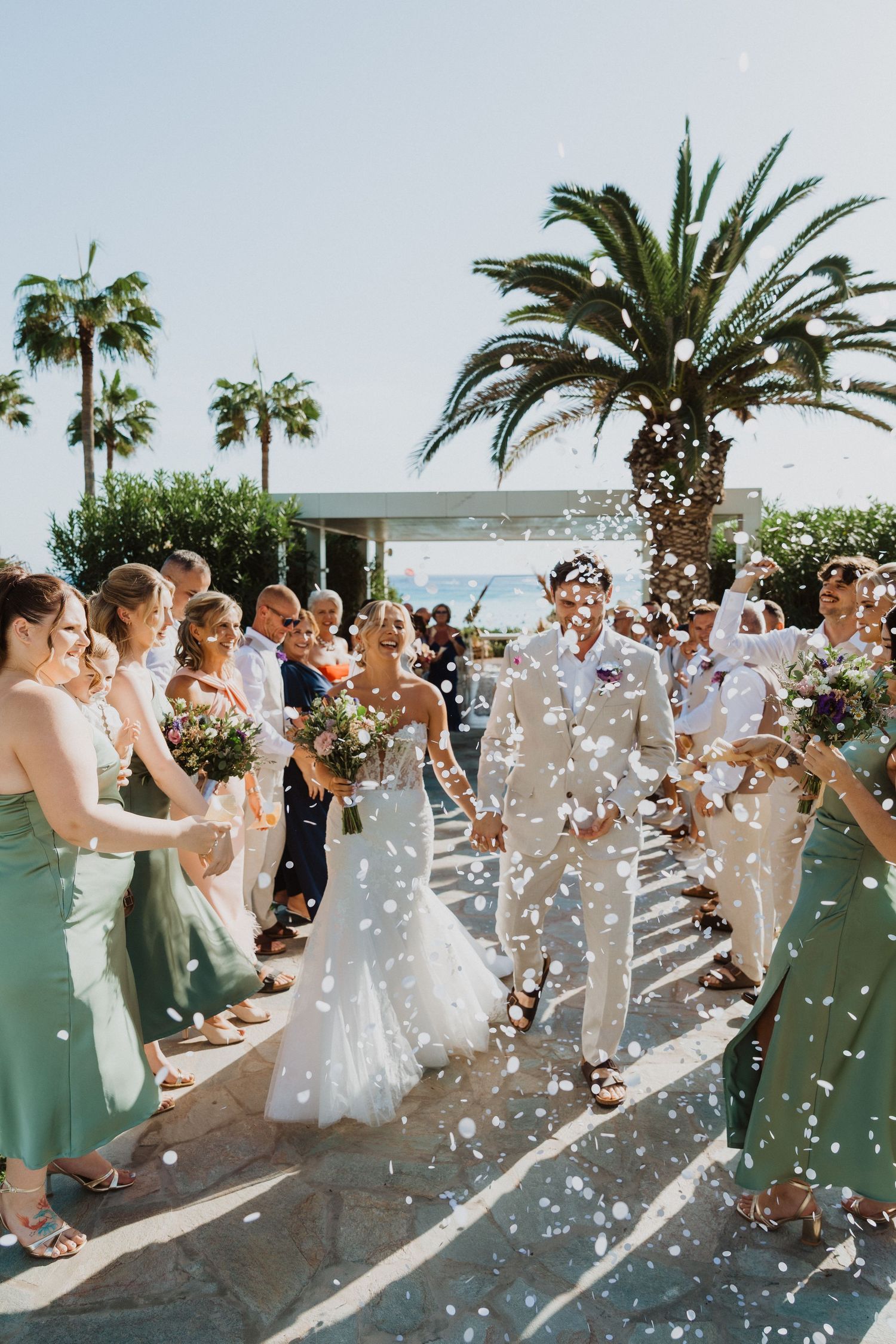 Wedding party walks through a shower of confetti at a tropical beach venue.