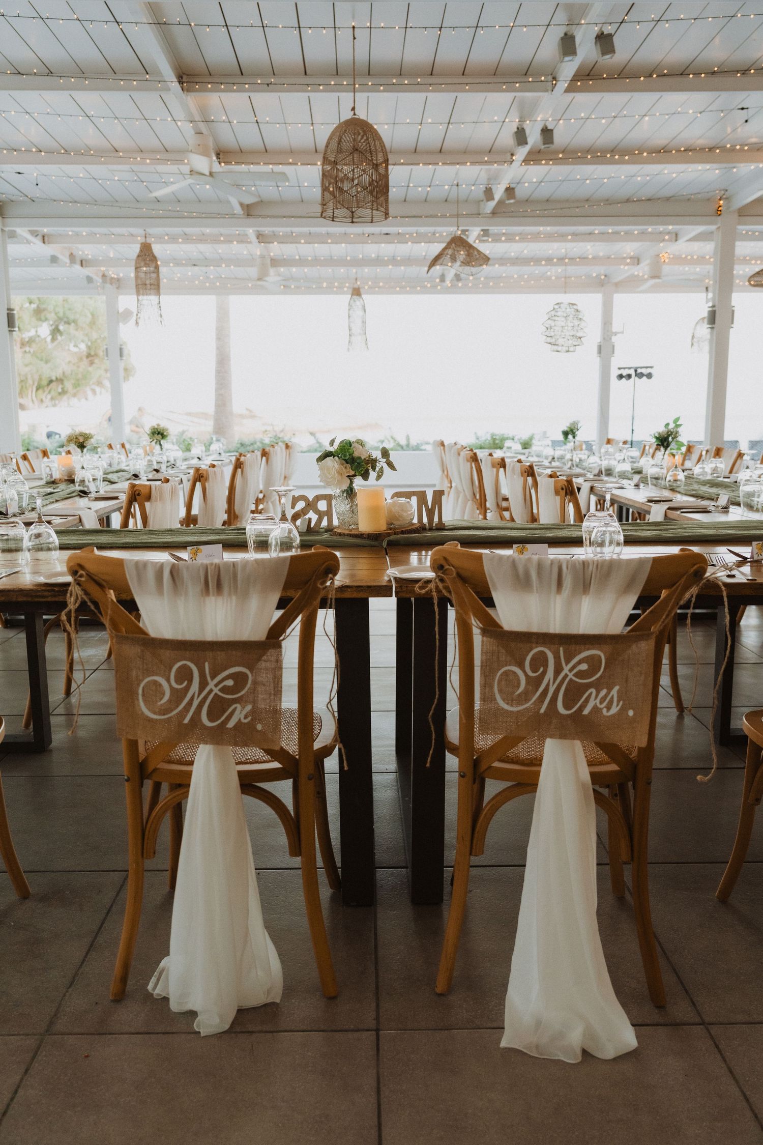 Wedding reception chairs marked with Mr and Mrs signs and white fabric draping.