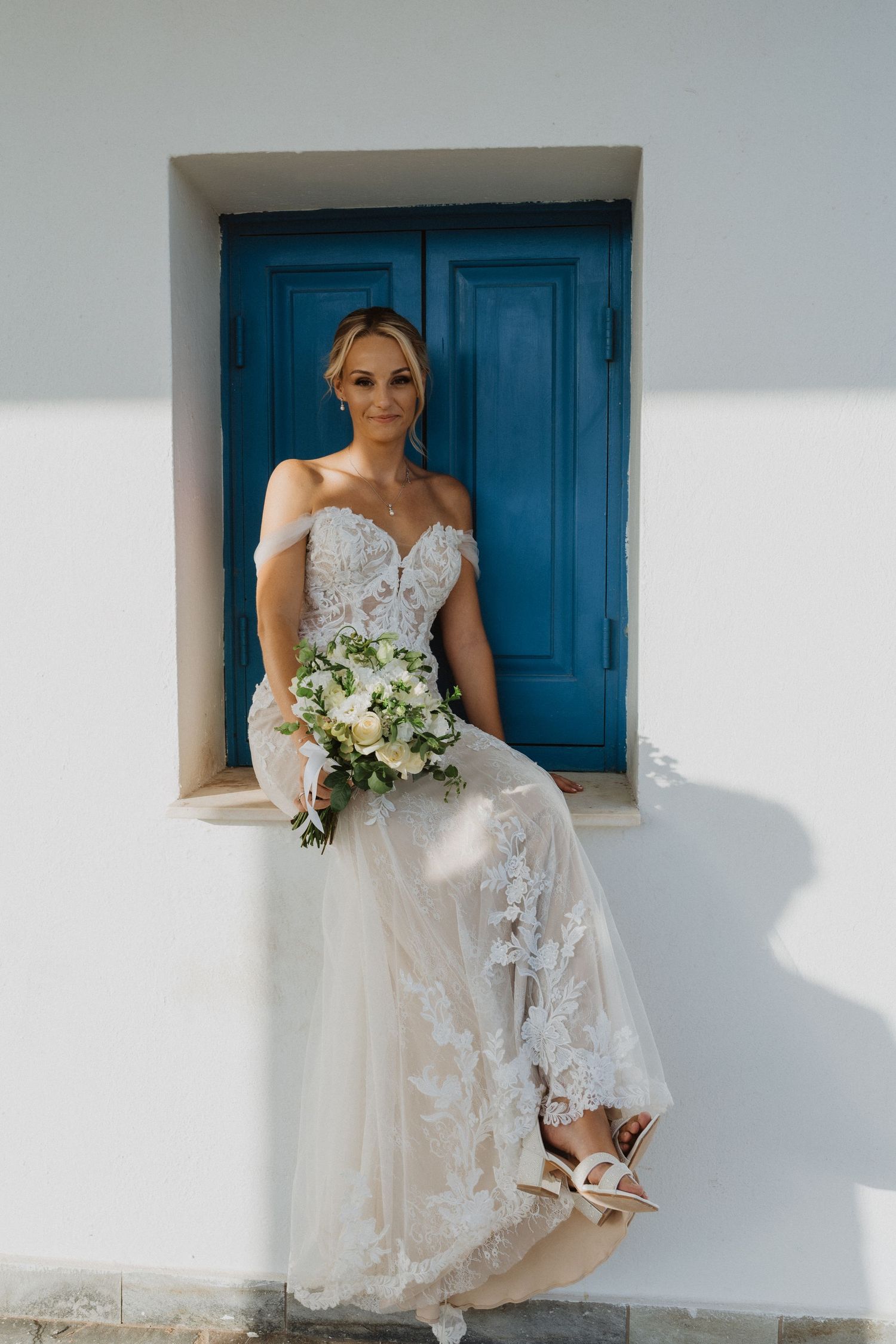 Elegant lace wedding dress details captured against white walls and blue doors.