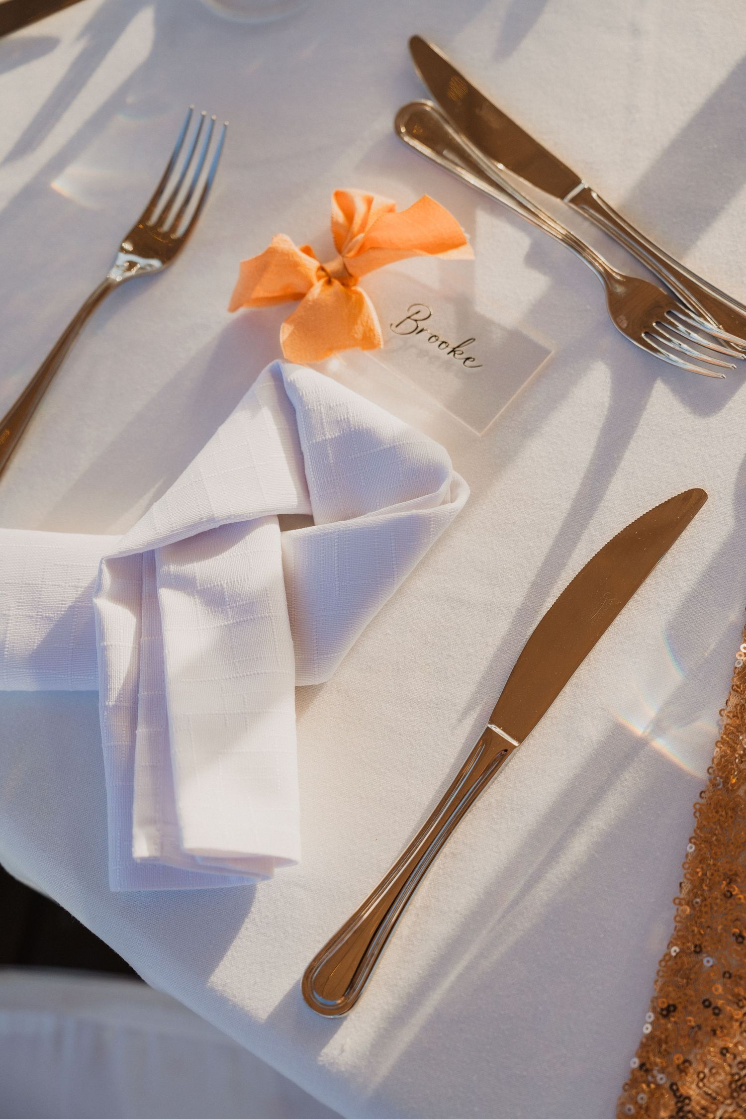 Place settings with white napkins and peach bows on a formal dining table.