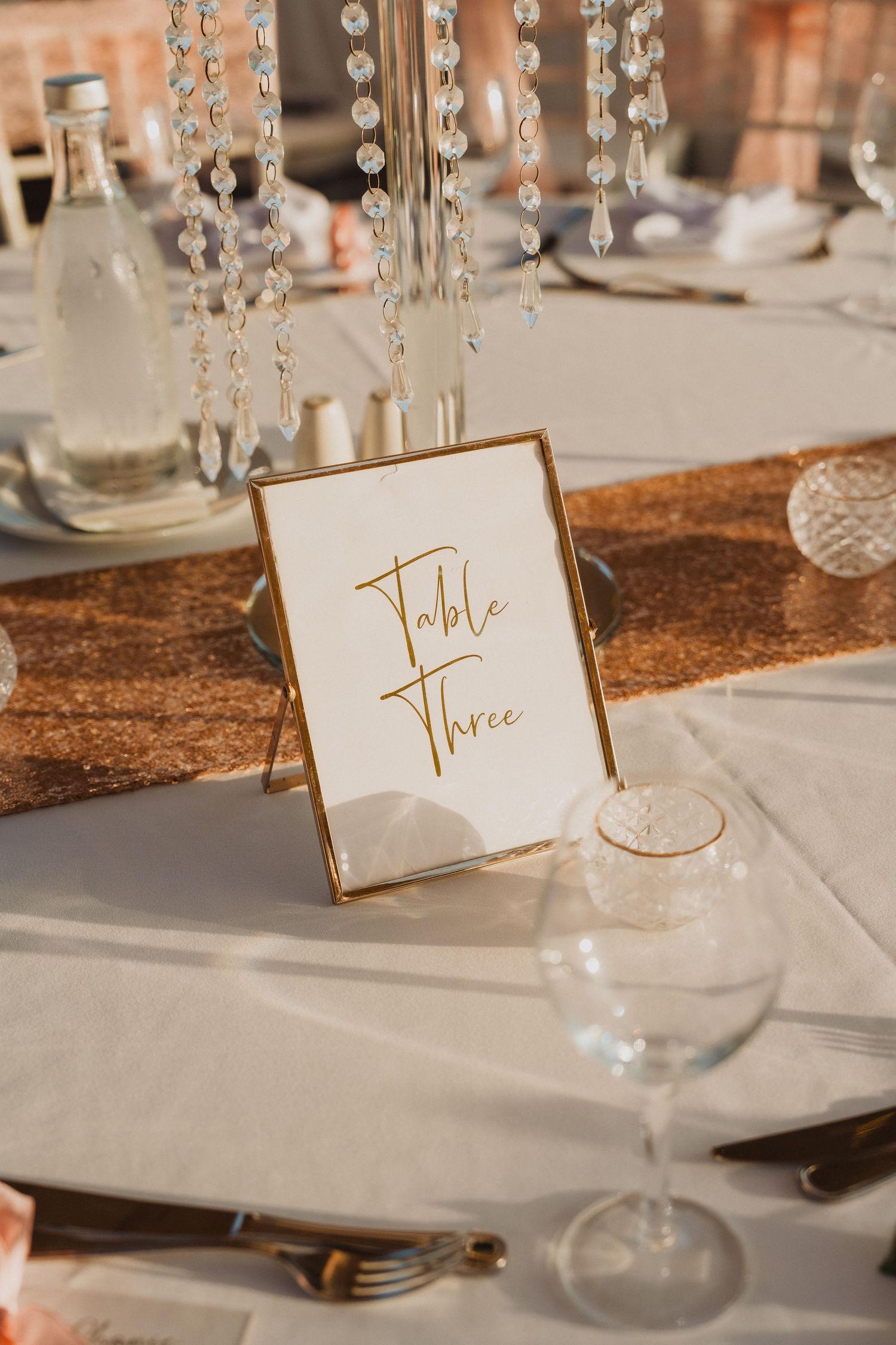 Elegant table settings with gold calligraphy table numbers and crystal decorations at wedding reception.