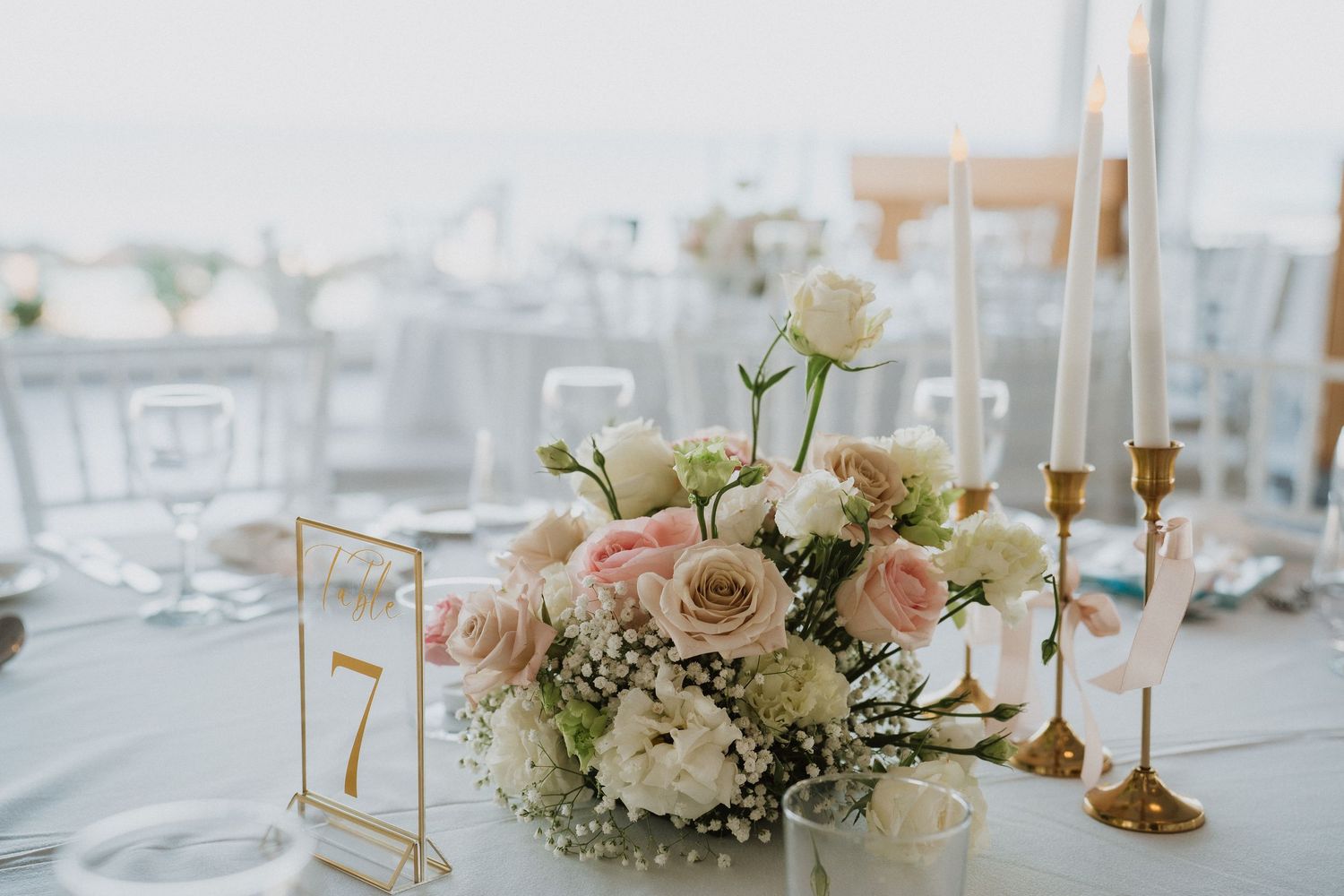Elegant wedding reception table settings with white floral centerpieces, gold candlesticks and soft romantic decor.