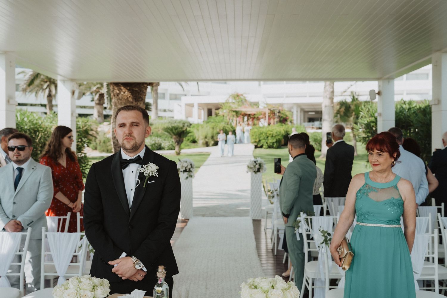 Groom in black tuxedo stands at altar awaiting bride during outdoor wedding ceremony.